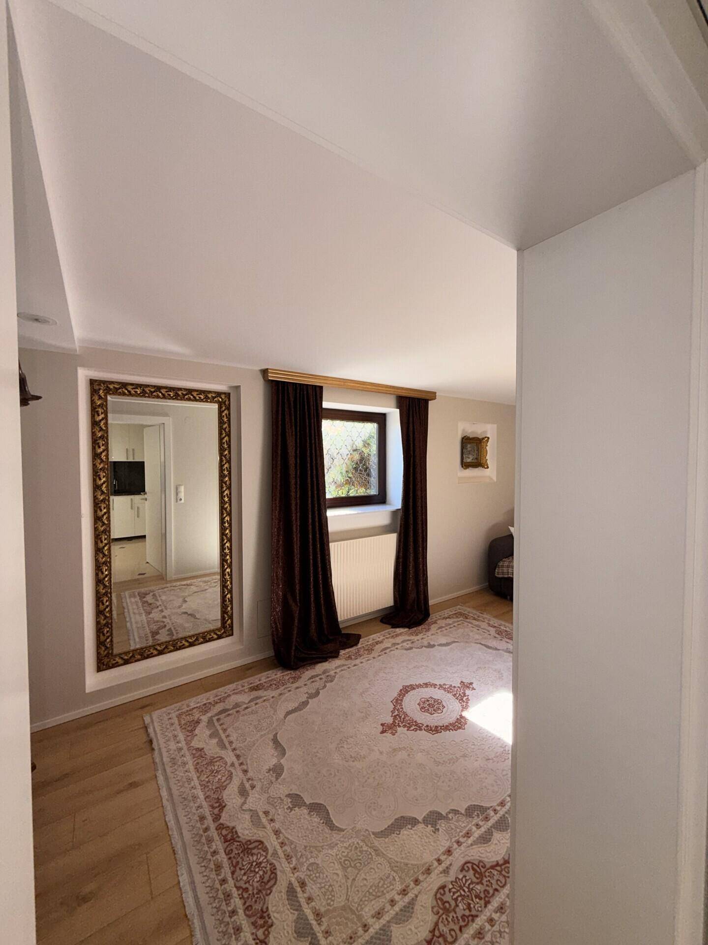 Geräumiger Wohnbereich mit großem Spiegel, Fenster und traditionellem Teppich.
