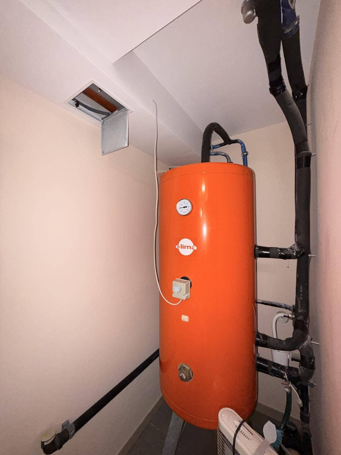 Hauswirtschaftsraum mit großem orangefarbenem Warmwasserspeicher und Rohrinstallationen.
