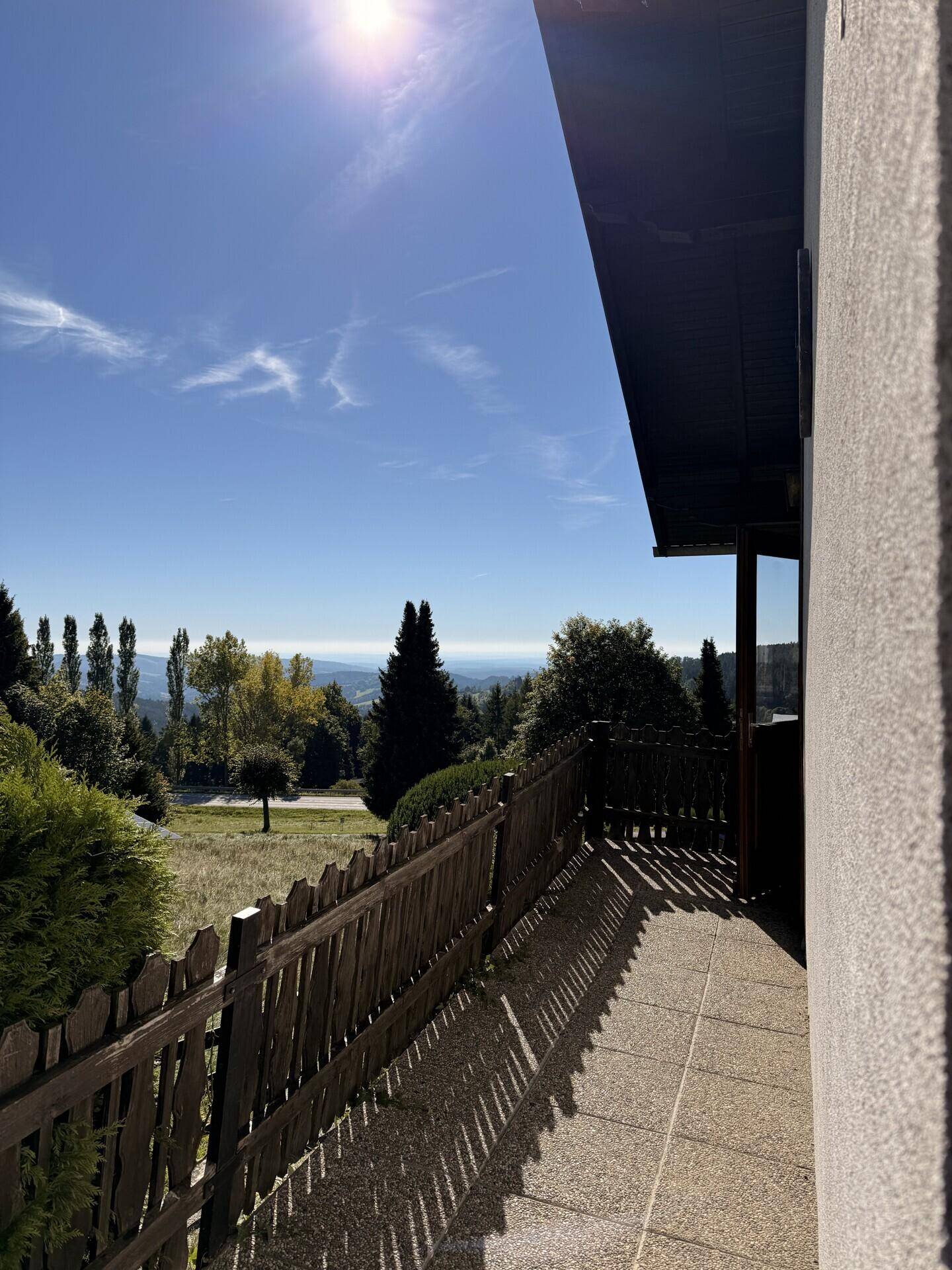 Sonniger Balkon mit Fliesenboden und weitem Blick über die grüne Landschaft bis zu den Bergen.