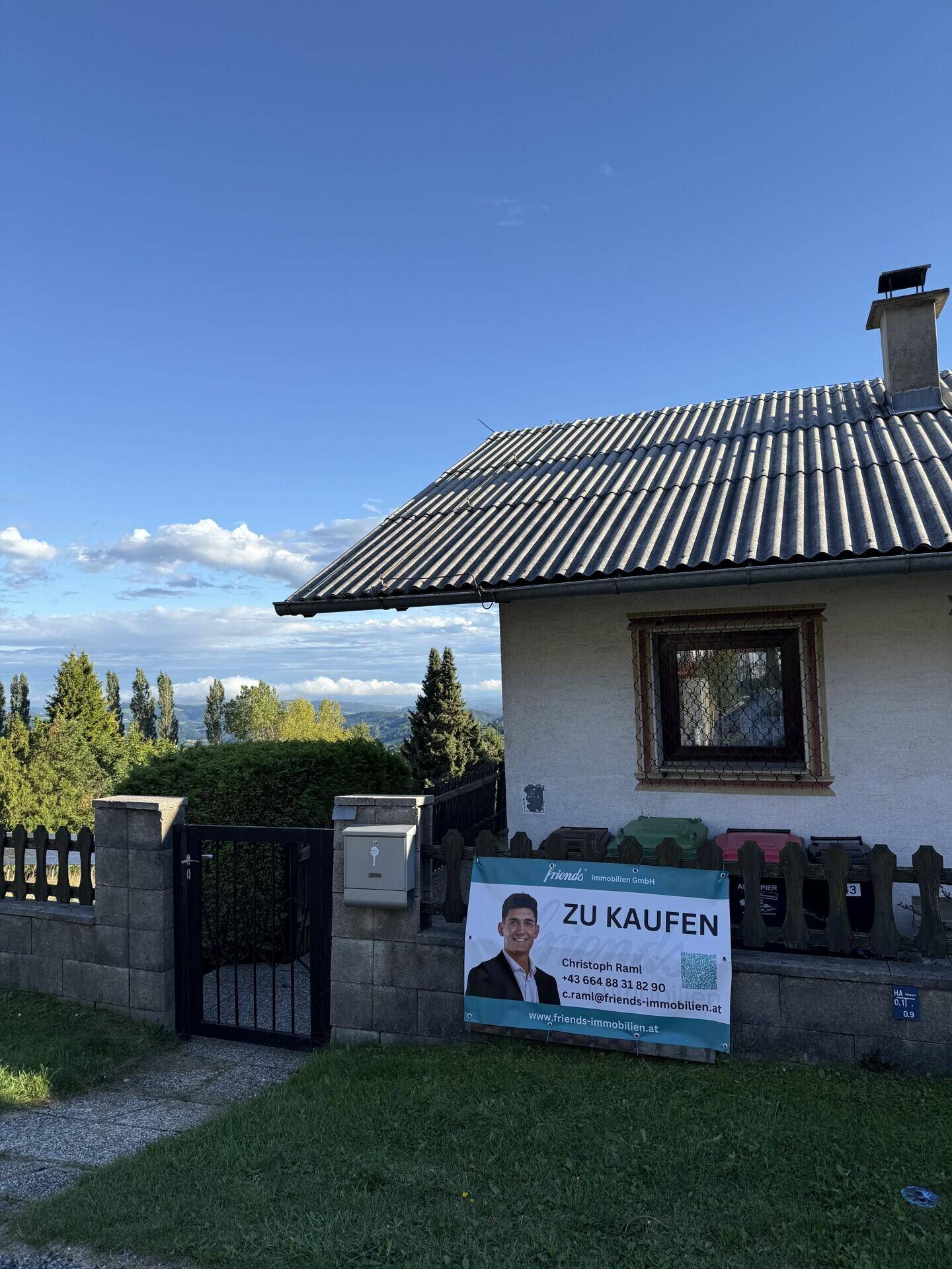 Hausfassade mit Satteldach und einem "Zu Kaufen"-Schild im Vorgarten.