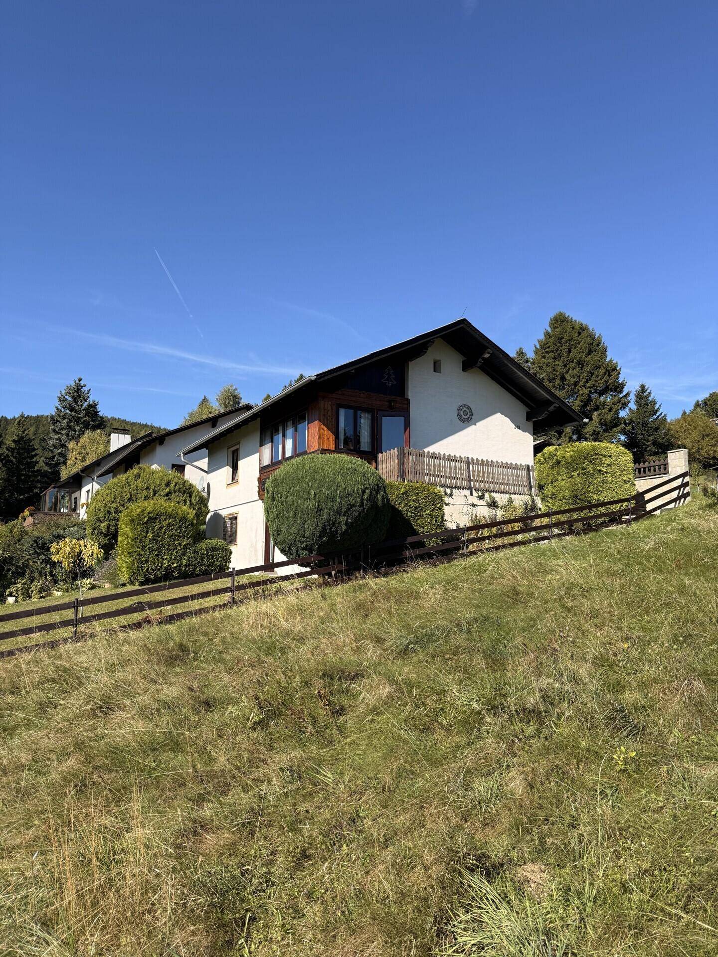 Das Haus eingebettet in die grüne Hanglandschaft, mit Balkon und gepflegter Fassade.