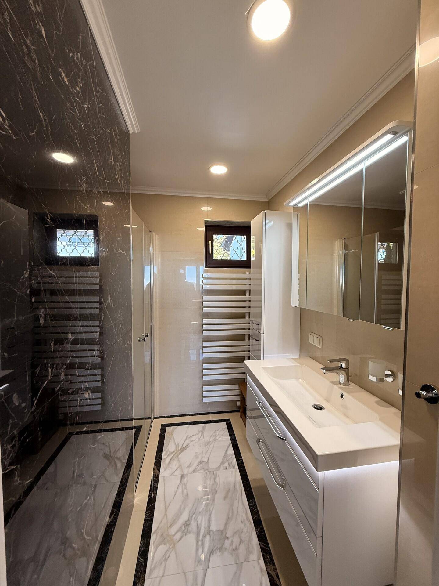 Modernes Badezimmer mit Marmoroptik-Fliesen, begehbarer Dusche und Waschtisch mit Spiegelschrank.