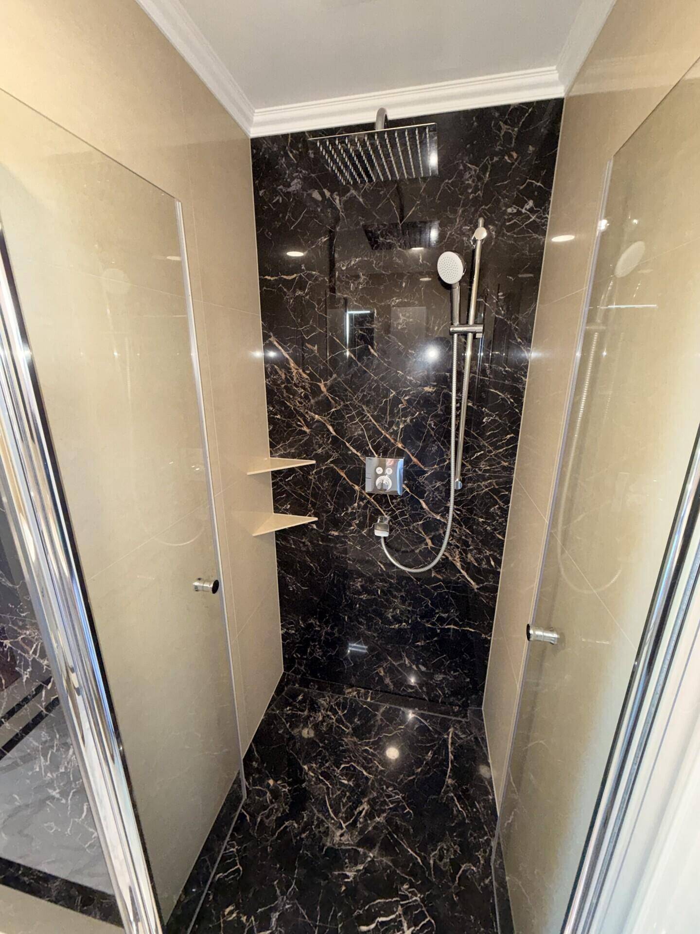 Elegante Duschkabine mit dunklen Marmorfliesen, Regendusche und Handbrause.