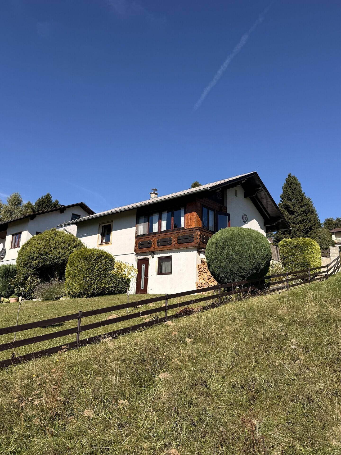 Das Haus von der Hangseite des Gartens aus gesehen, mit Holzzaun und Balkon.