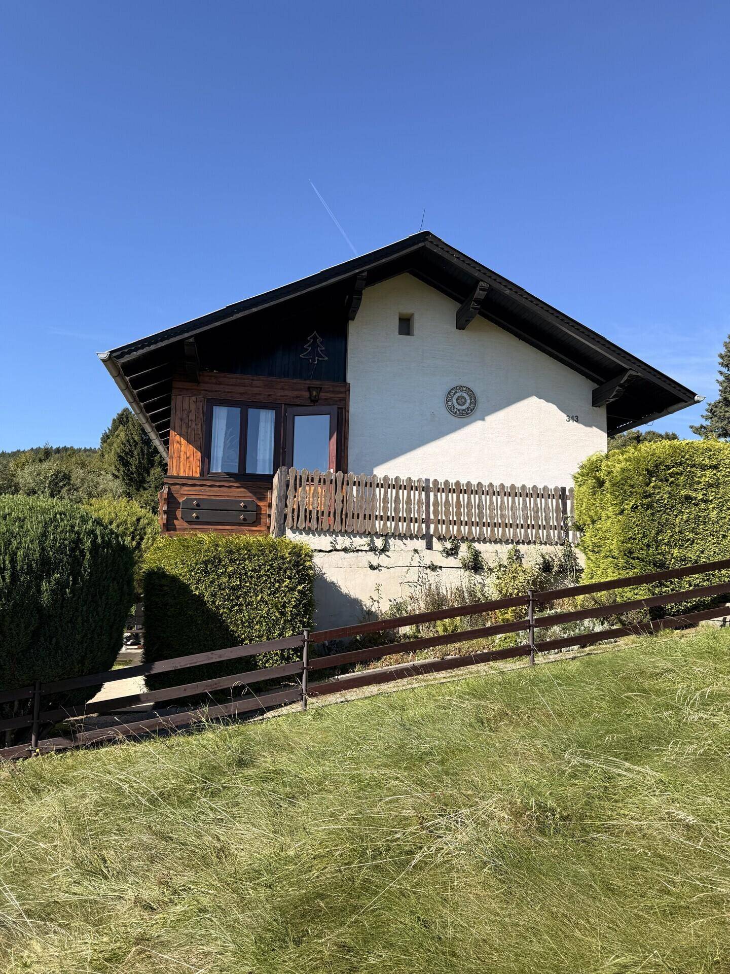Seitenansicht des Hauses mit Holzverkleidung, Balkon und traditionellem Holzzaun.