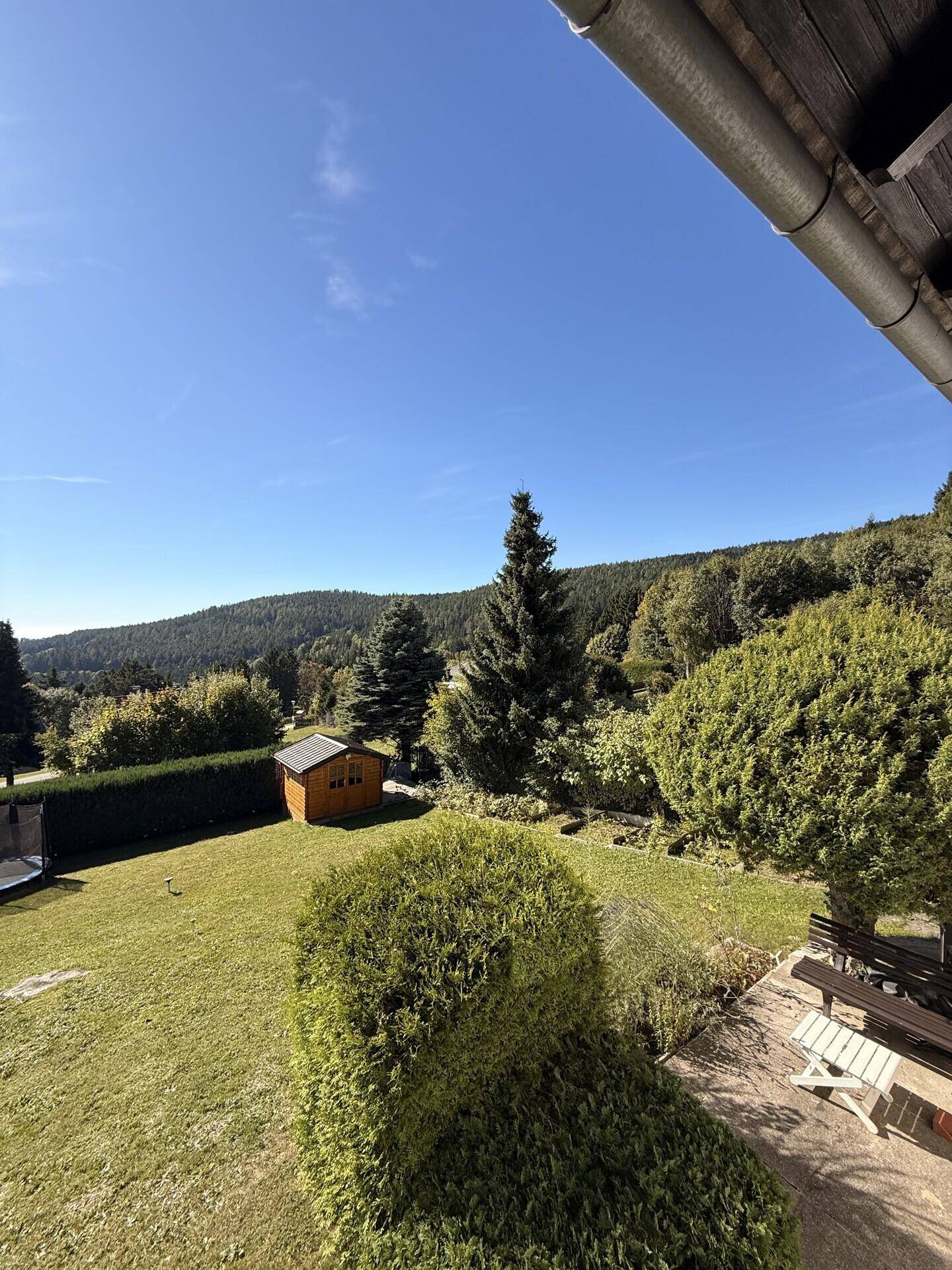 Gepflegter Garten mit Rasen, Hecken und einem kleinen Gartenhaus in ländlicher Umgebung.