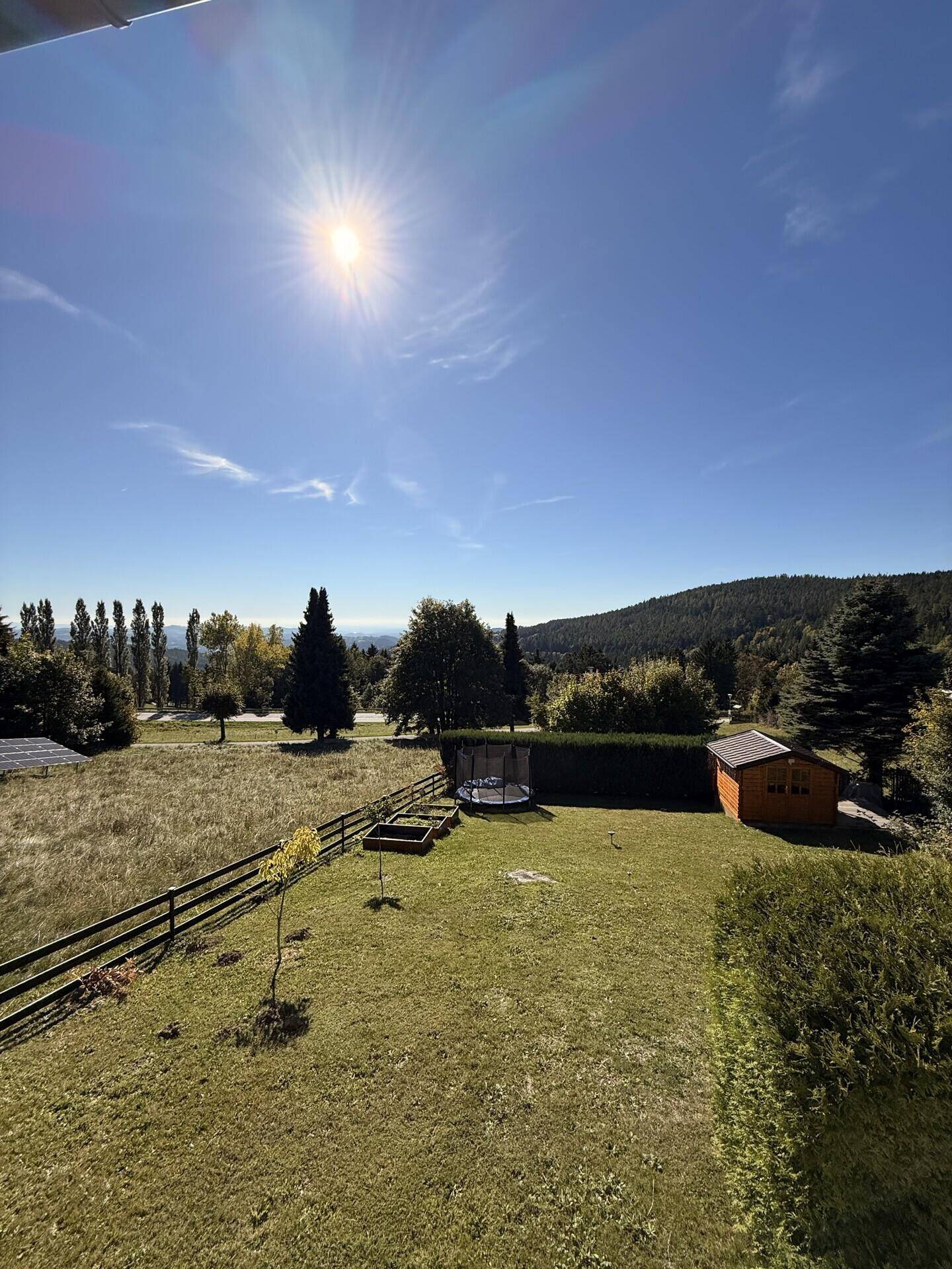 Sonniger Blick vom Balkon auf den gepflegten Garten mit Trampolin und Gartenhaus.
