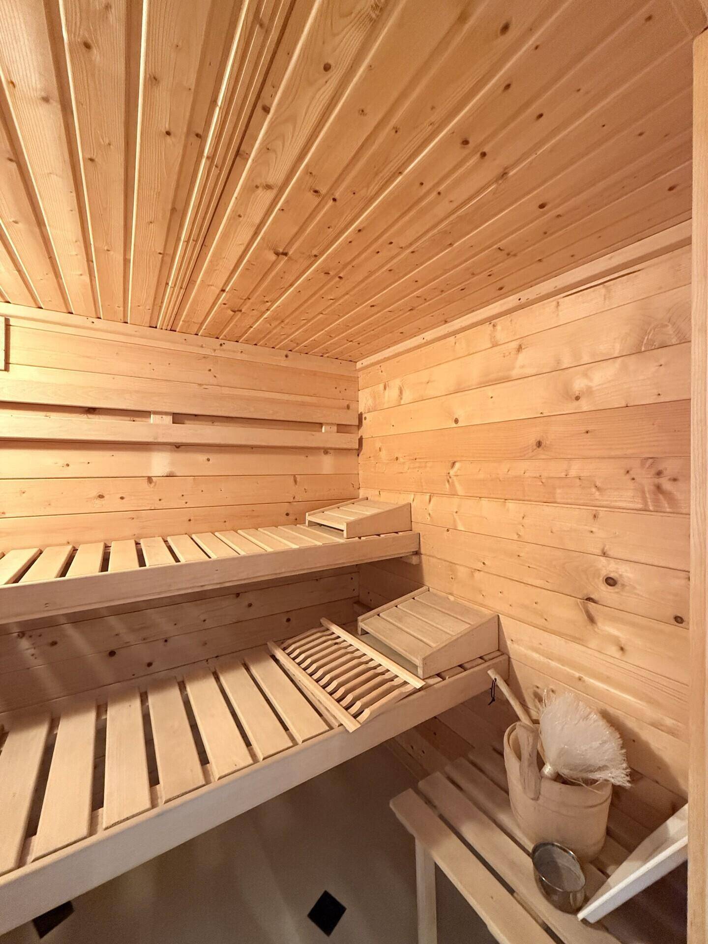 Geräumige Holzsauna mit bequemen Bänken und traditionellem Sauna-Zubehör für Entspannung.