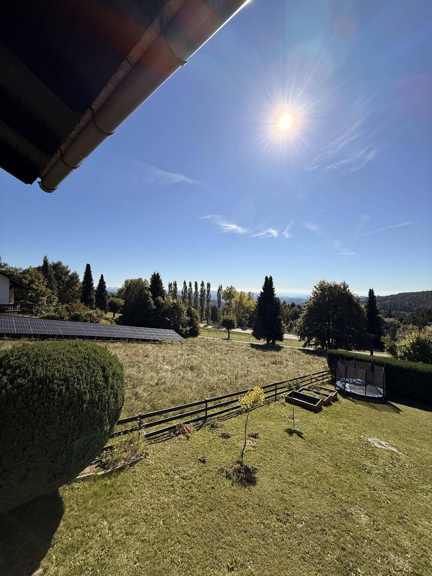 Sonniger Garten mit Rasenfläche, Bäumen und Blick auf die umliegende Landschaft.