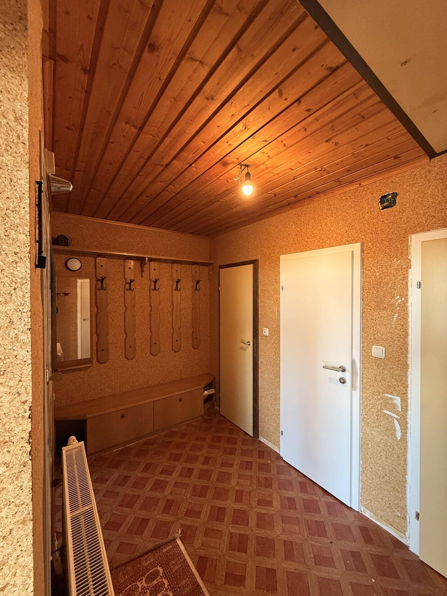 Eingangsbereich mit Holzbalkendecke, Garderobe und Linoleumboden.