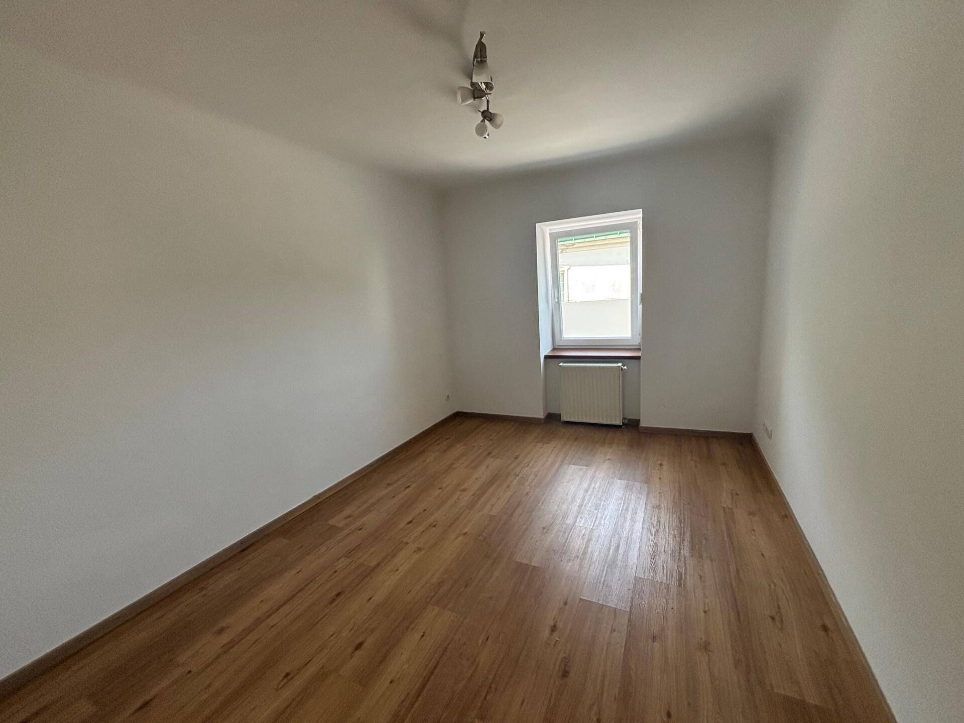 Leeres Schlafzimmer mit Laminatboden und einem Fenster, bereit zur individuellen Gestaltung.