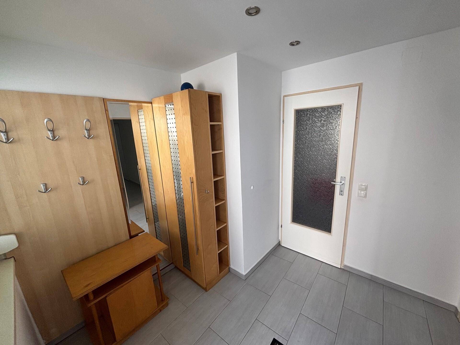 Heller Flur mit Garderobe, Spiegelschrank und gefliestem Boden am Eingangsbereich.