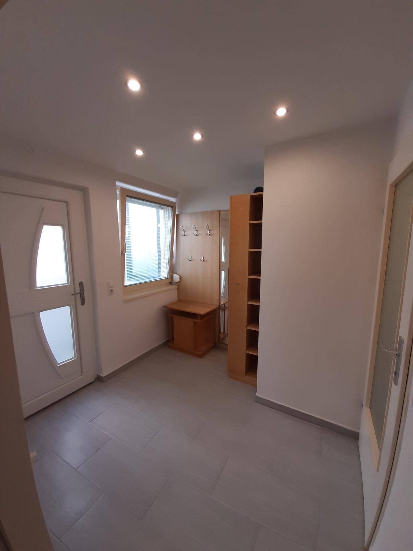 Eingangsbereich mit heller Fliesenboden, Einbauschränken und einem Fenster für Tageslicht.