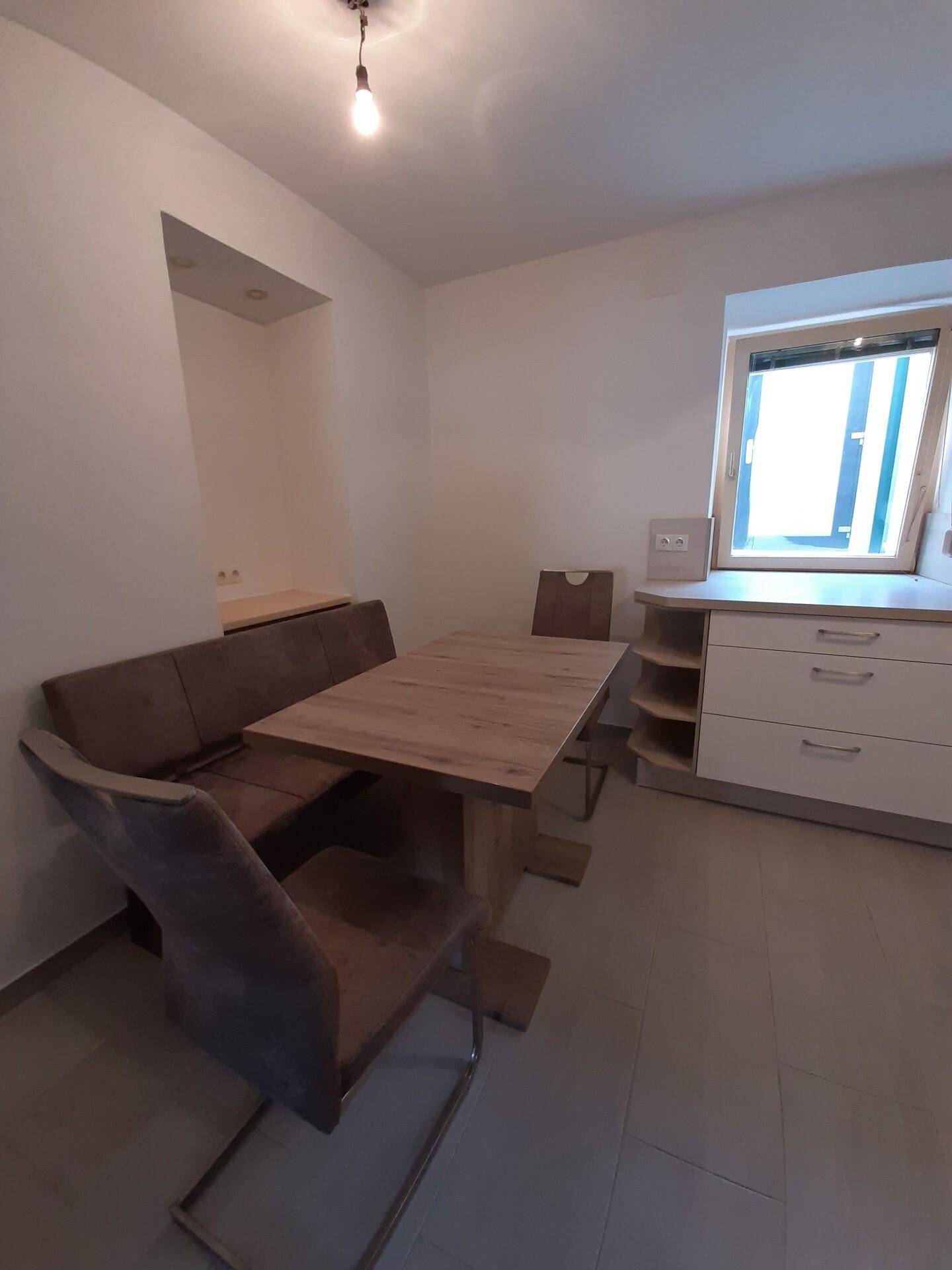 Gemütlicher Essbereich mit Holztisch, Eckbank und Stühlen neben einem Fenster.