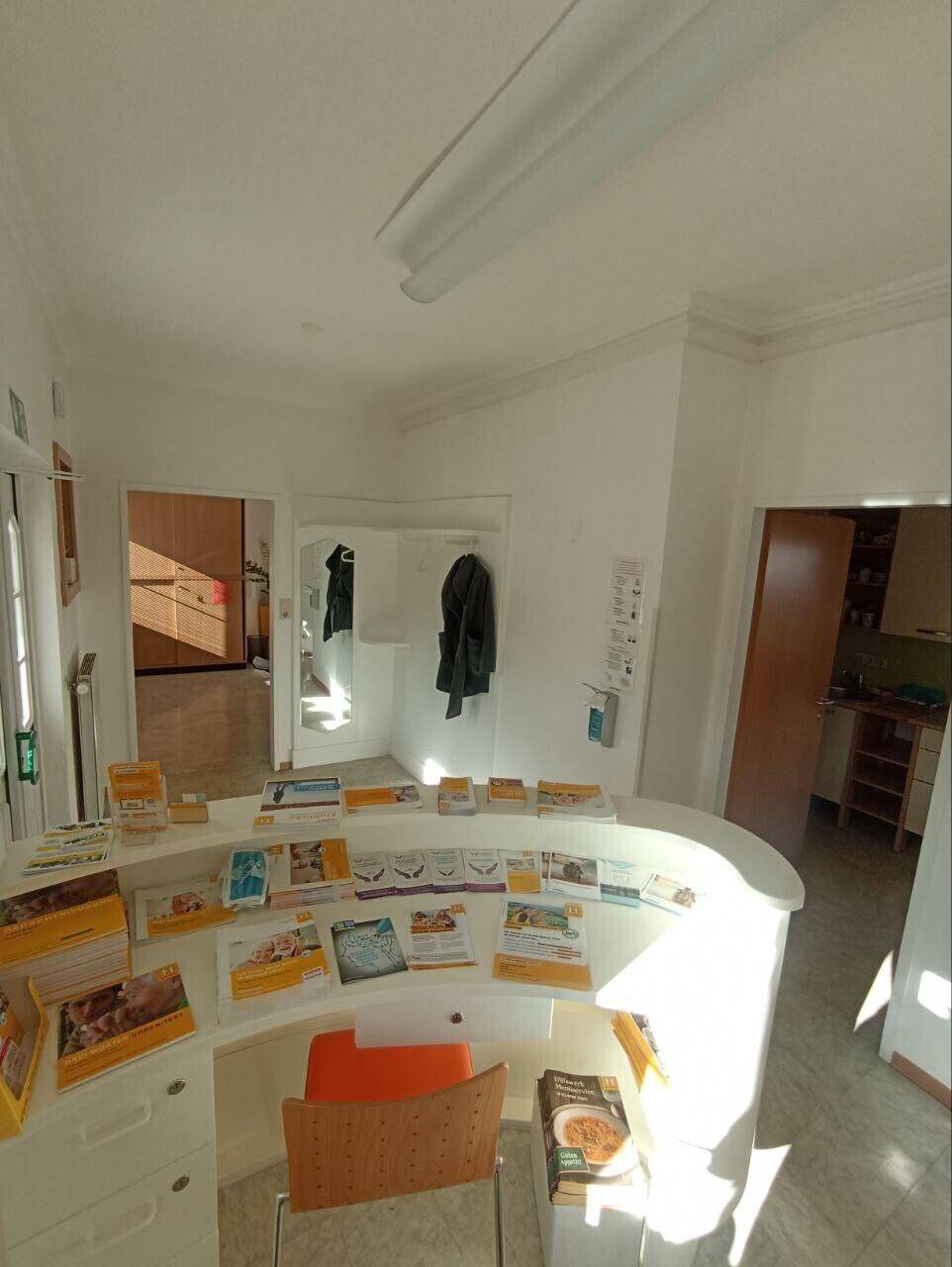 Empfangsbereich mit geschwungener Theke, Informationsmaterialien und Bürostuhl.