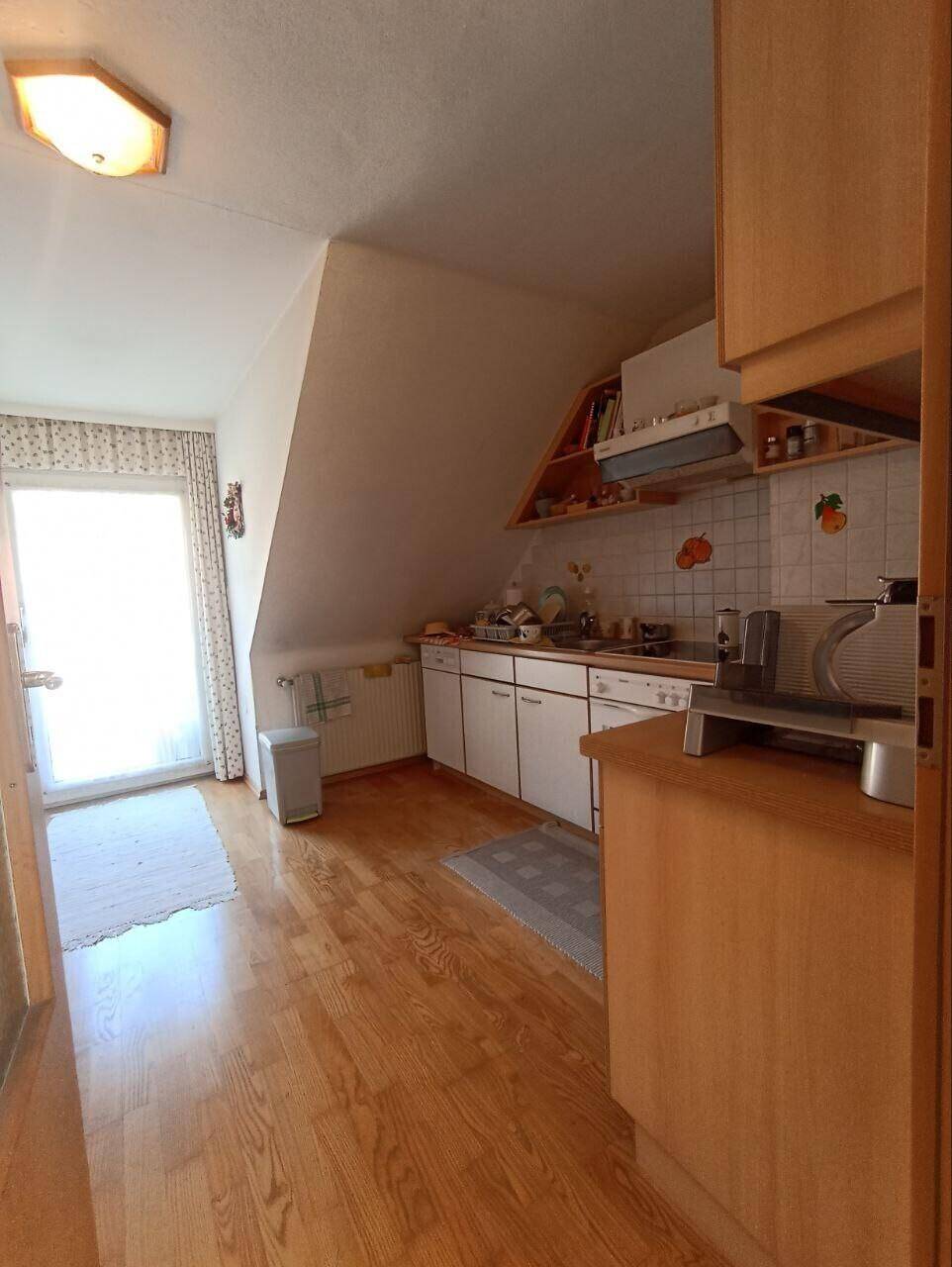 Dachgeschossküche mit schräger Decke, Holzboden und Zugang zu einem Balkon oder einer Terrasse.
