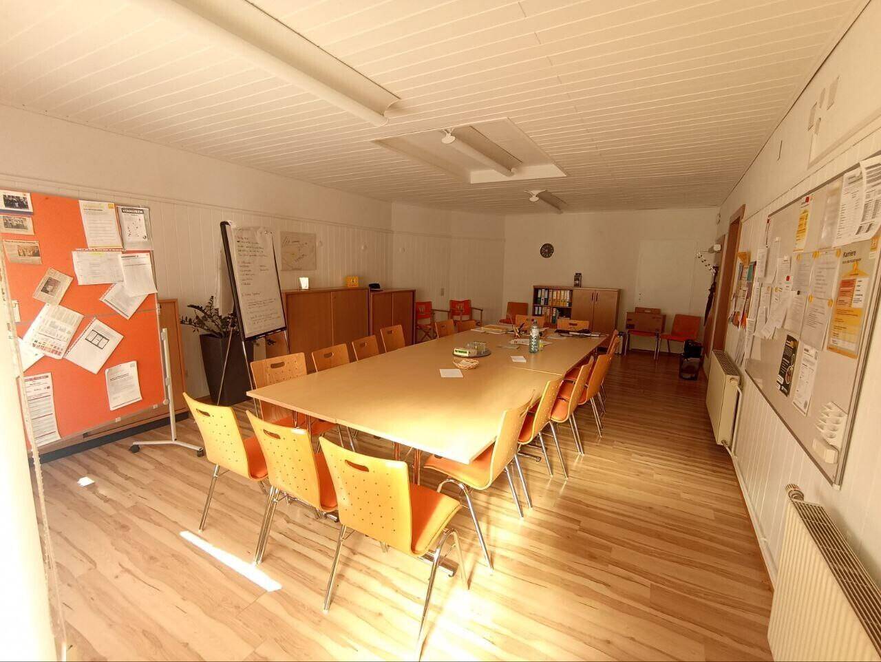 Großer Besprechungsraum mit langem Holztisch und zahlreichen orangefarbenen Stühlen.