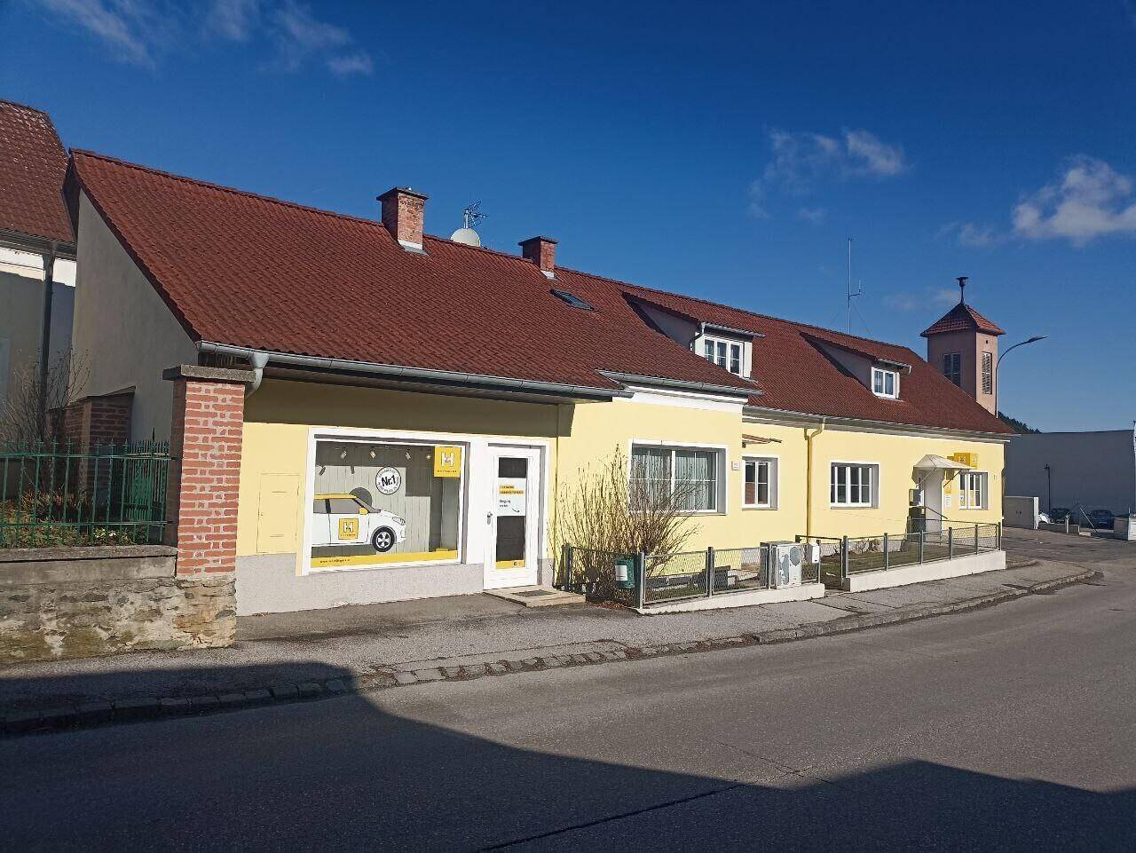 Gelbes Gebäude mit rotem Ziegeldach und mehreren Fenstern an einer Straße gelegen.