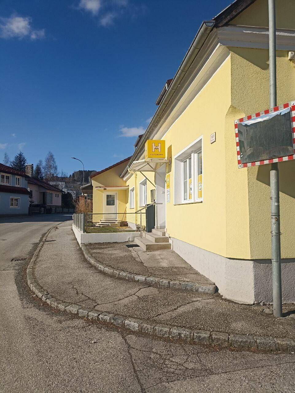 Seitenansicht des gelben Gebäudes von einer Straßenecke aus mit Gehweg.