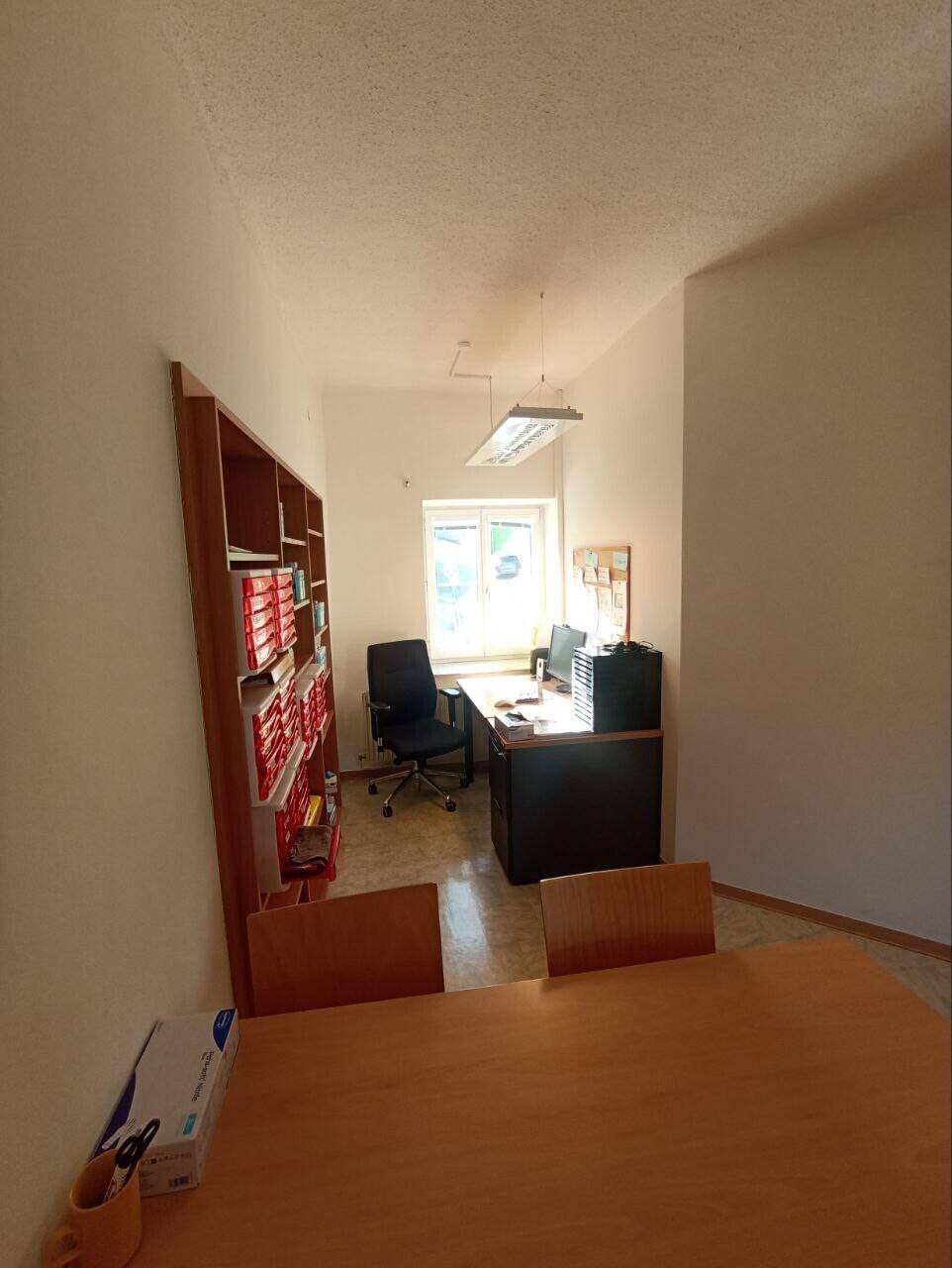 Büroraum mit Schreibtisch, Bürostuhl und einem Bücherregal an der Wand.