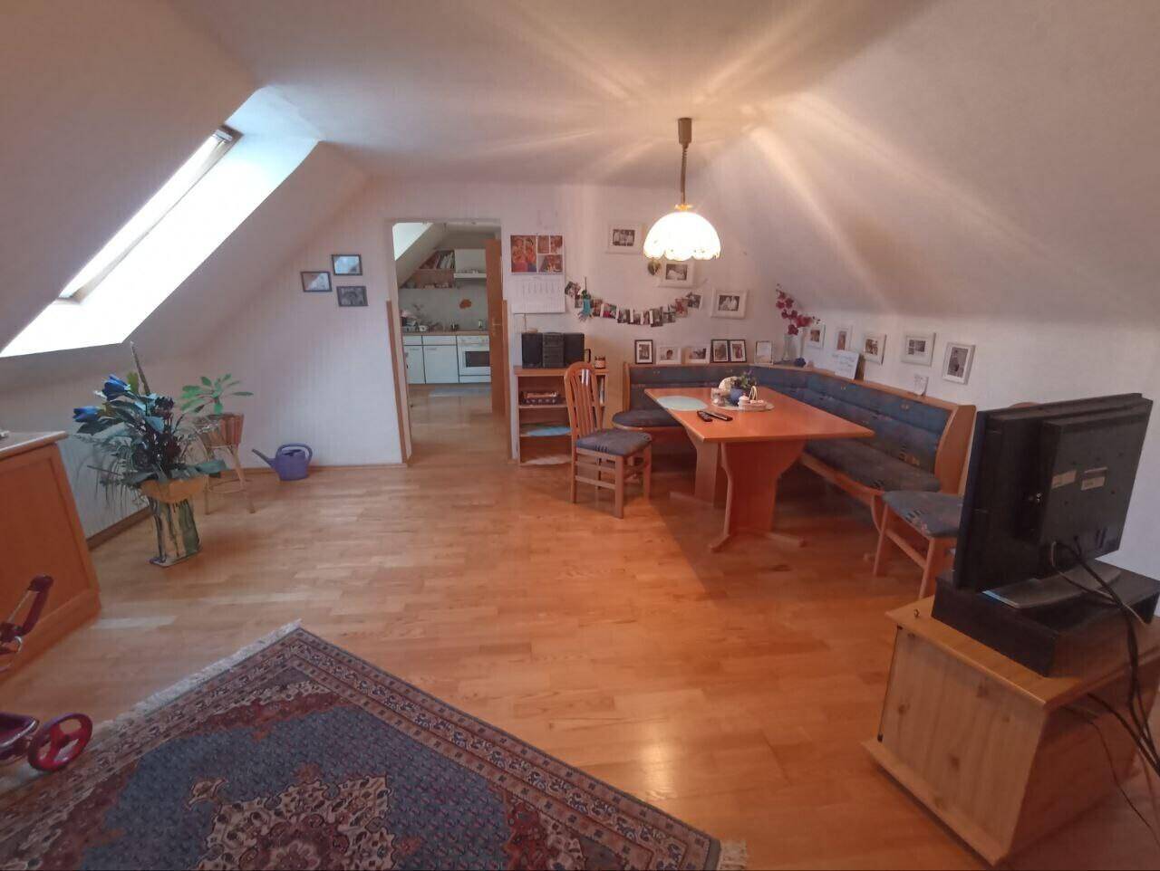 Dachgeschoss-Wohnbereich mit Essgruppe, Sofa und Blick in die angrenzende Küche.