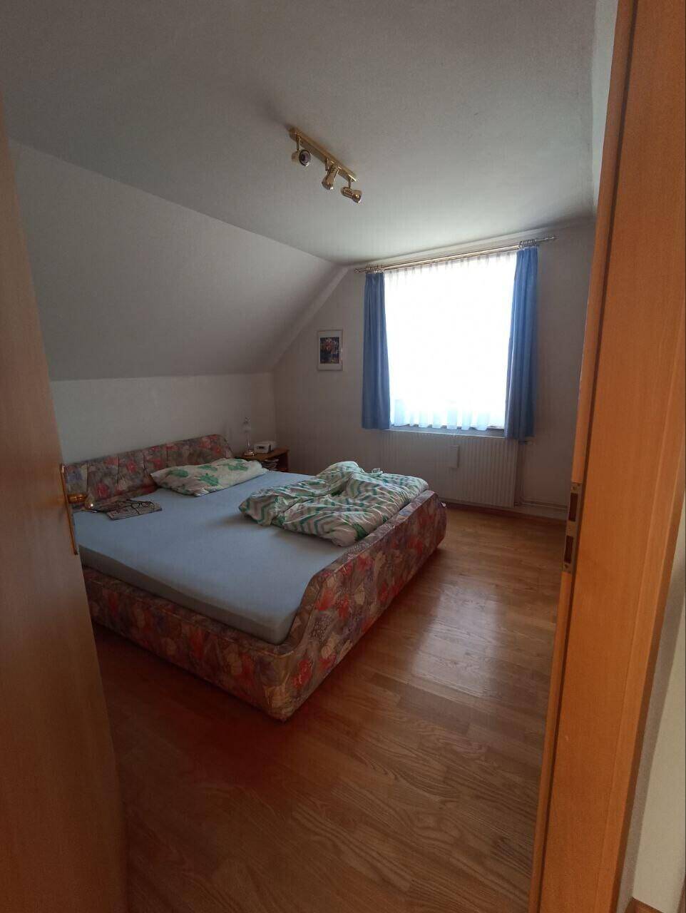 Helles Schlafzimmer im Dachgeschoss mit Holzboden und einem großen Fenster für natürliches Licht.
