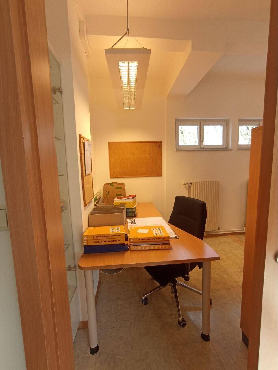 Arbeitsplatz in einem Büro mit Schreibtisch, Büchern und einem Deckenlicht.