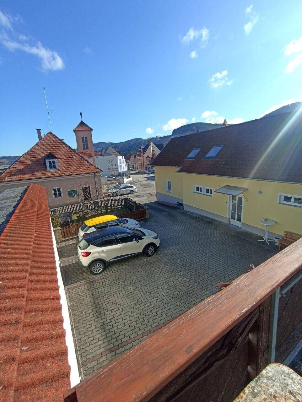 Blick von oben auf einen gepflasterten Innenhof mit parkenden Autos und umliegenden Gebäuden.