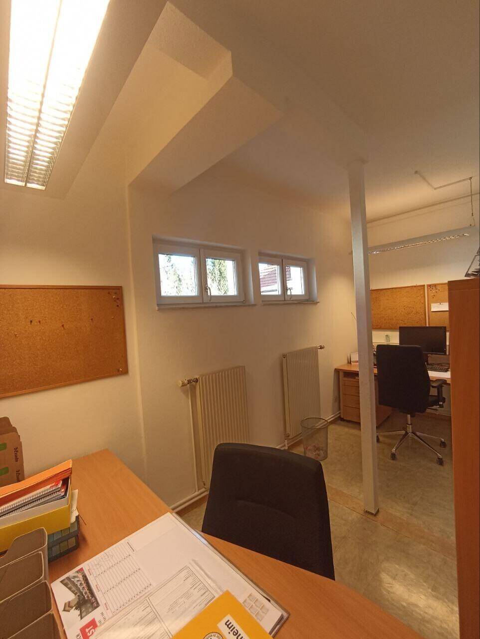 Büroarbeitsplatz mit Schreibtisch, Bürostuhl und kleinen Fenstern für Tageslicht.