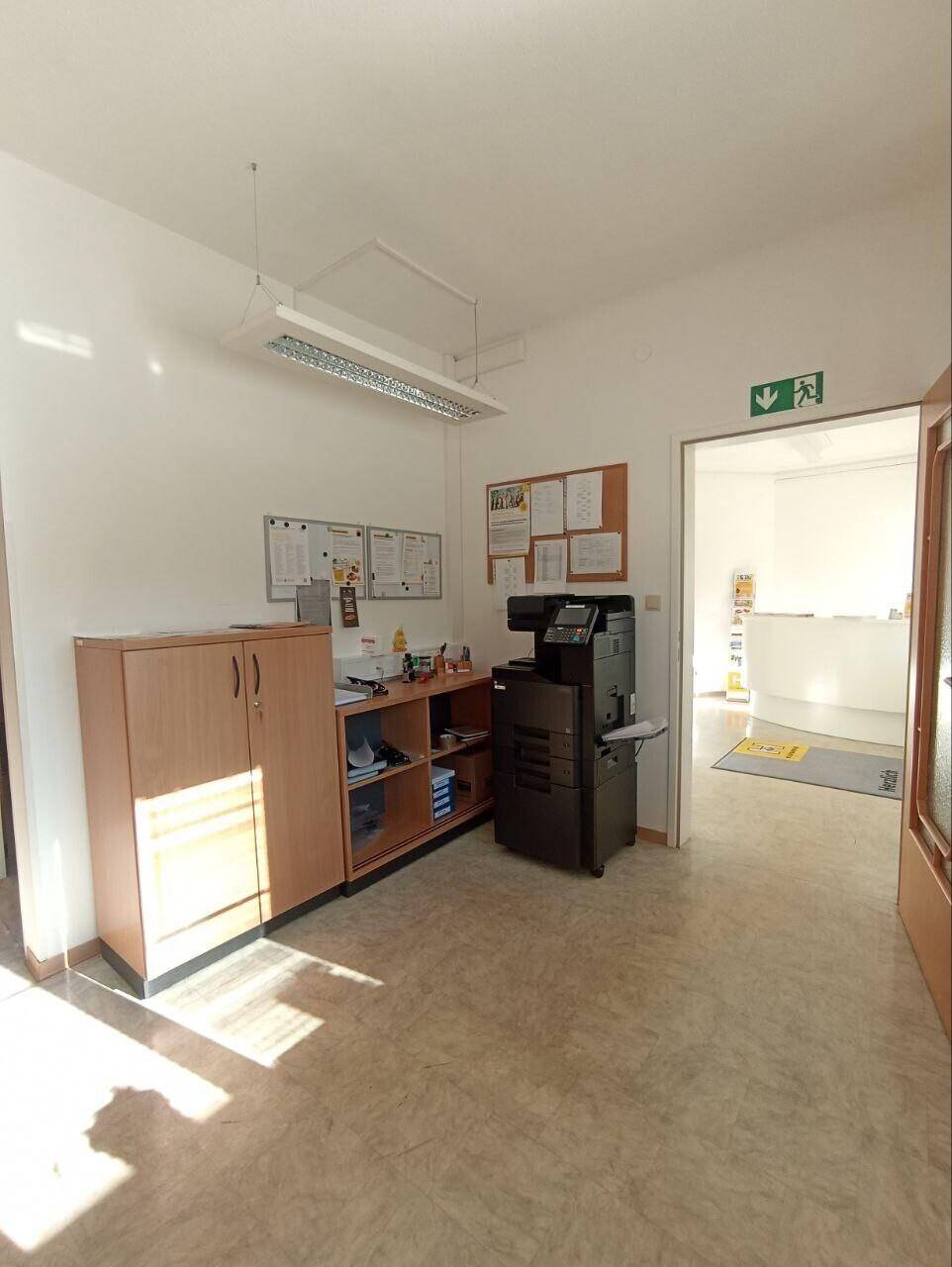 Büroraum mit Schreibtisch, Aktenschrank und großem Multifunktionsdrucker.