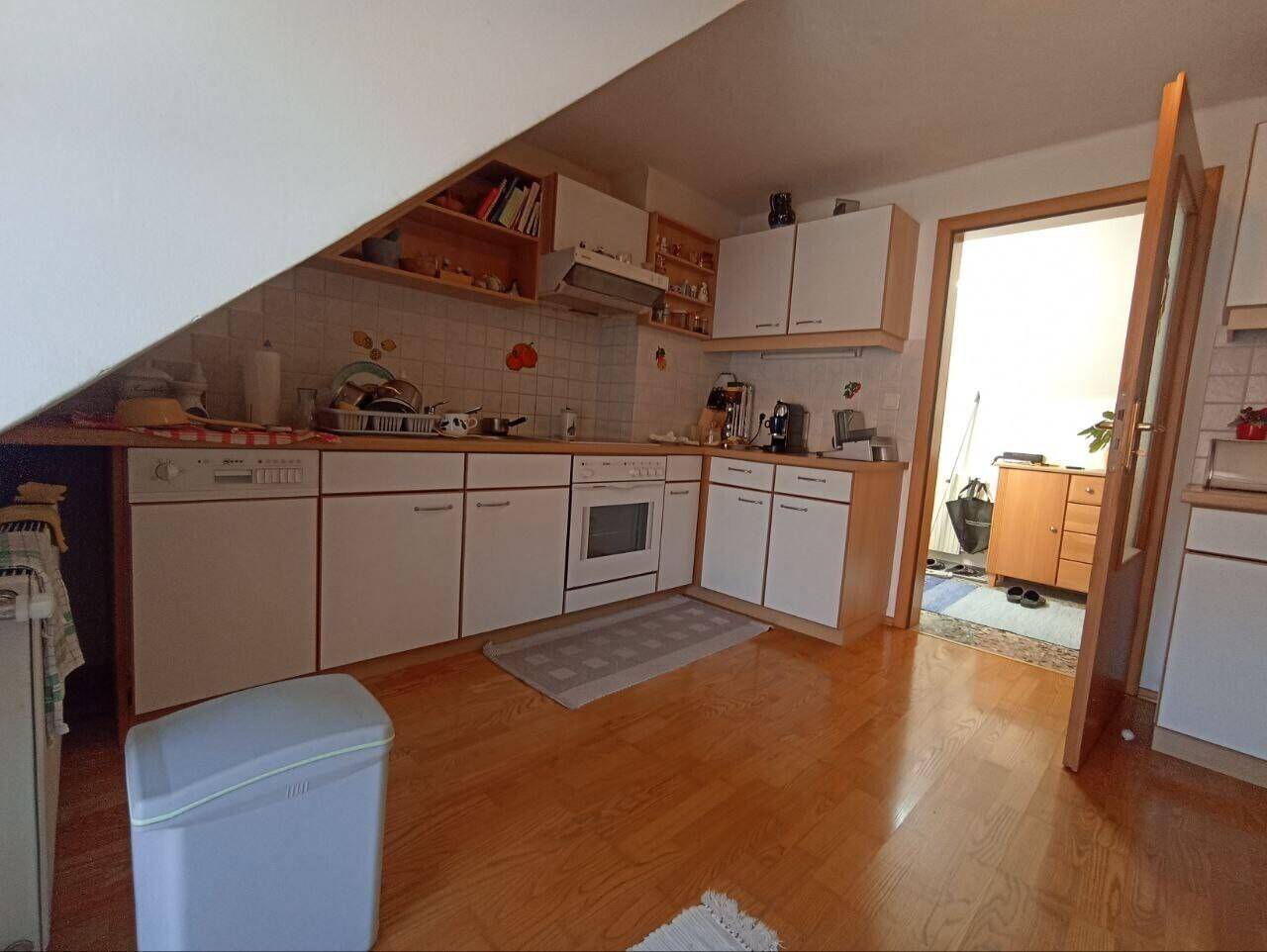Funktionale Küche im Dachgeschoss mit weißen Einbauschränken, Holzboden und Dachschräge.