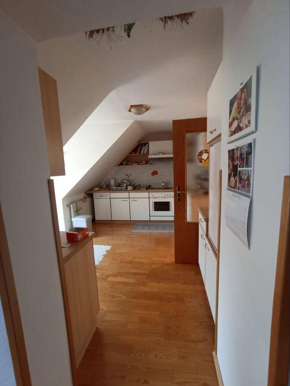 Flur mit Holzboden und Dachschräge, der zur Küche führt und einen Blick in den Raum bietet.