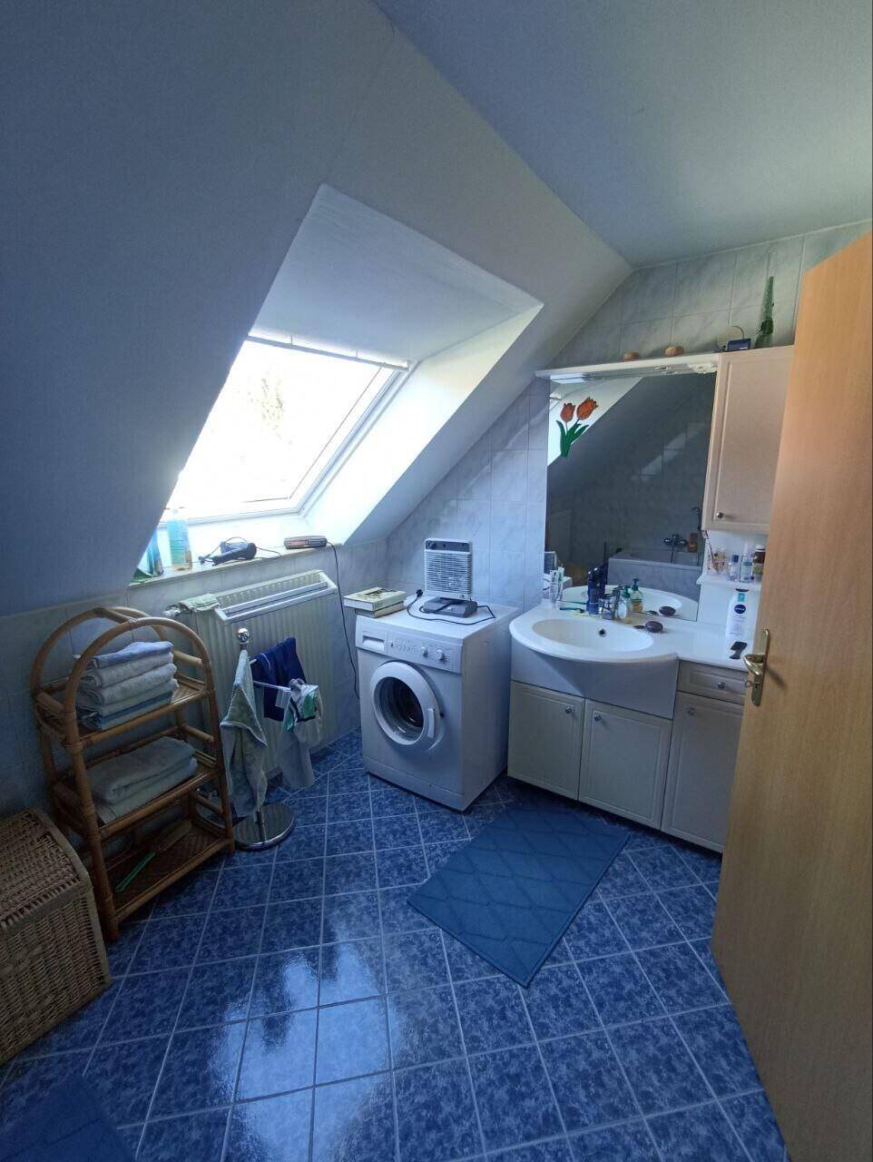 Badezimmer mit blauen Fliesen, Waschmaschine und einem Dachfenster für Tageslicht.