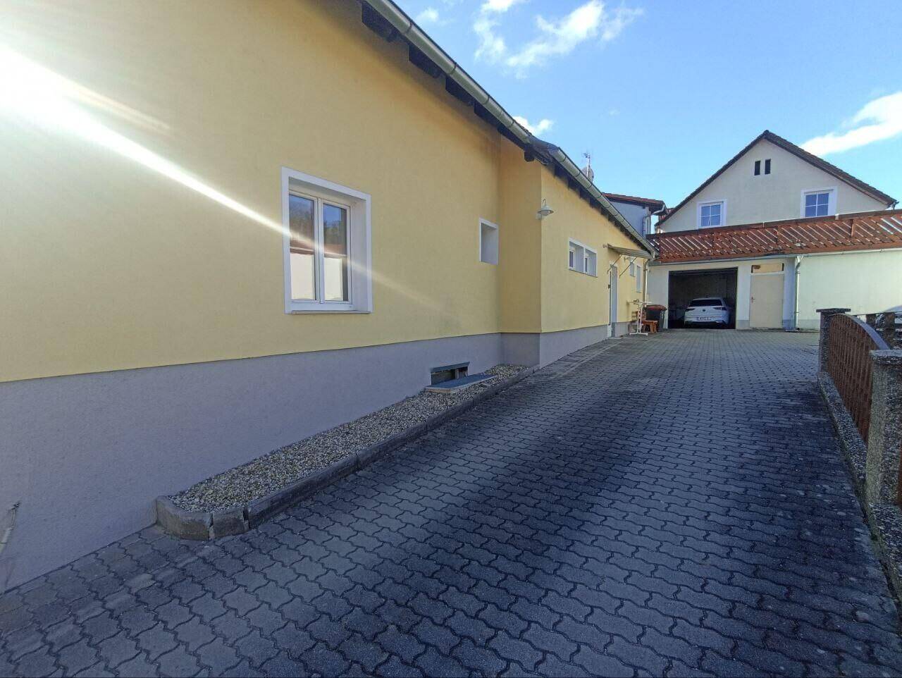 Seitenansicht des Gebäudes mit gepflasterter Zufahrt und einem Garagenbereich im Hintergrund.