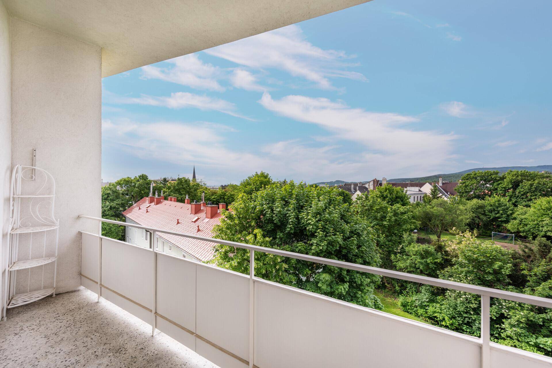 Heller Balkon mit weißem Geländer und weitem Blick über grüne Bäume und Dächer.