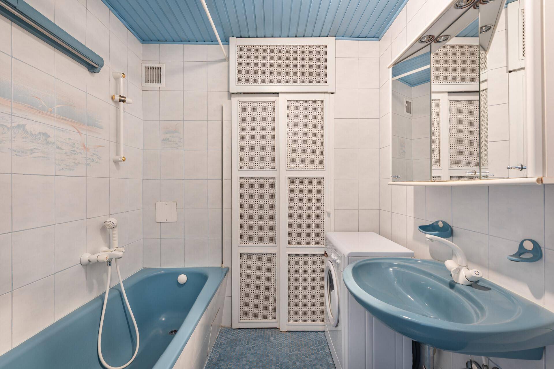 Badezimmer mit blauer Badewanne, passendem Waschbecken und weißen Fliesen im 80er-Jahre-Stil.