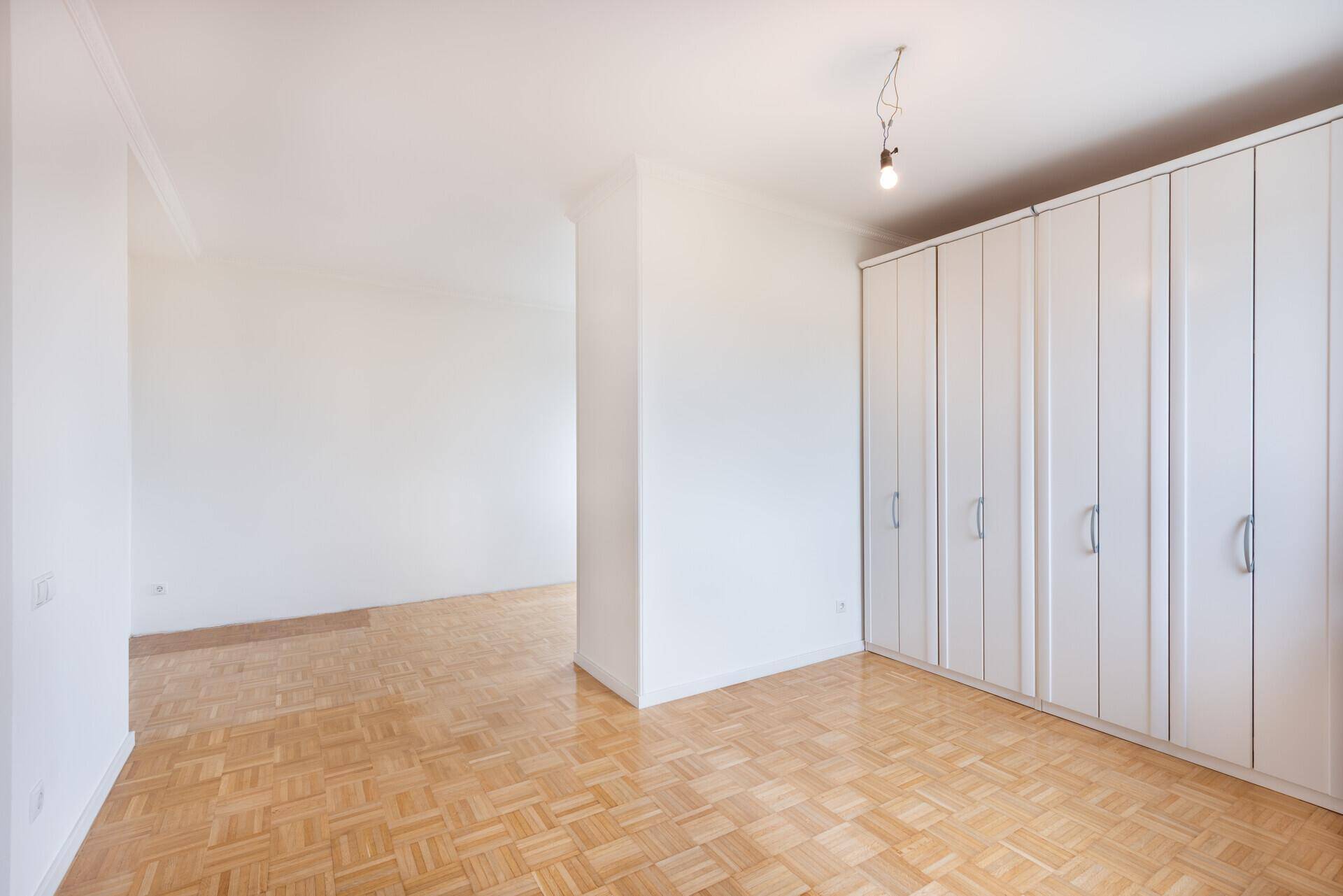 Geräumiges Zimmer mit Parkettboden und praktischen weißen Einbauschränken.