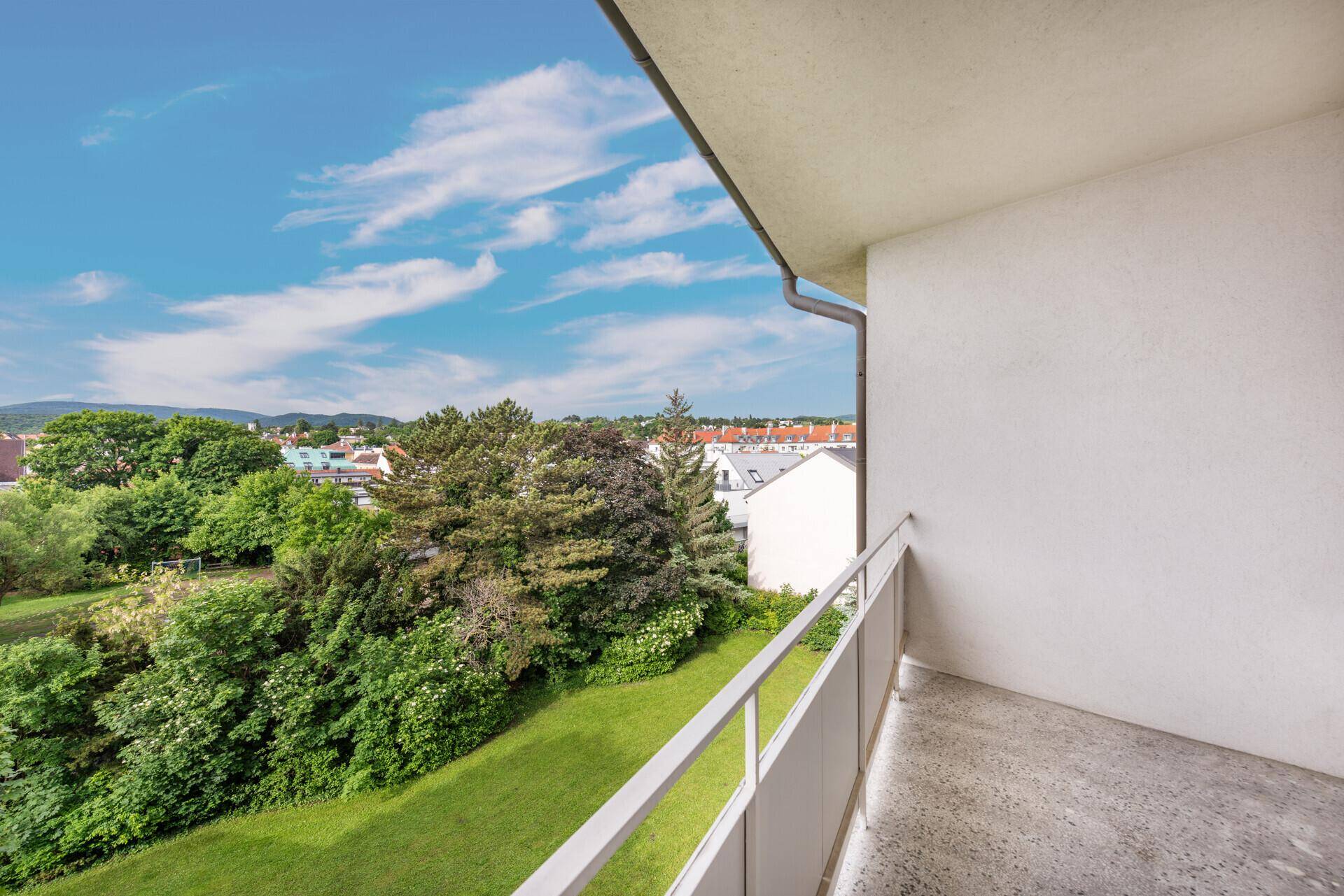 Balkon mit Blick ins Grüne und auf die umliegenden Gebäude unter blauem Himmel.