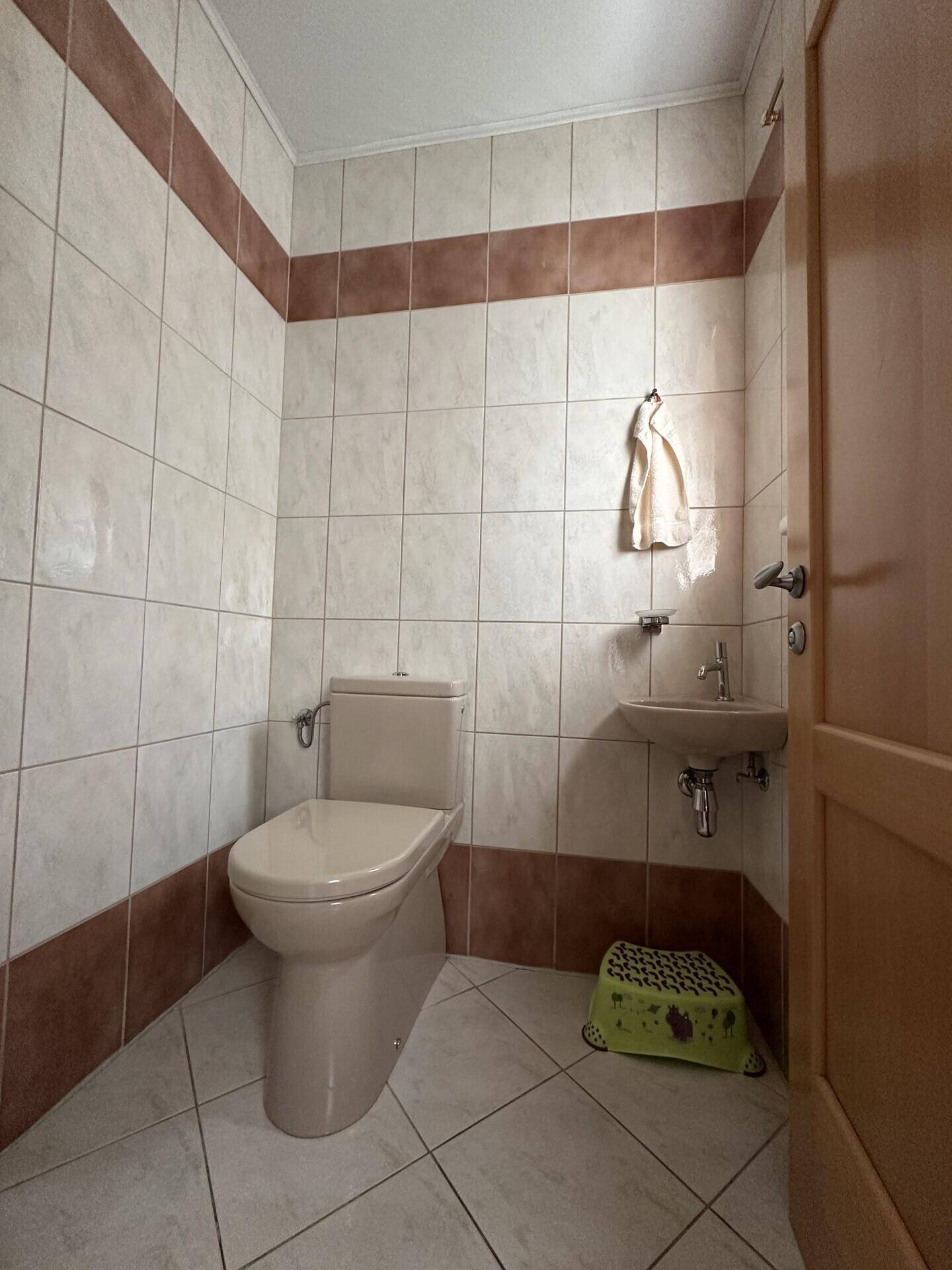 Kleines Gäste-WC mit beigefarbenen Fliesen und einem Waschbecken.