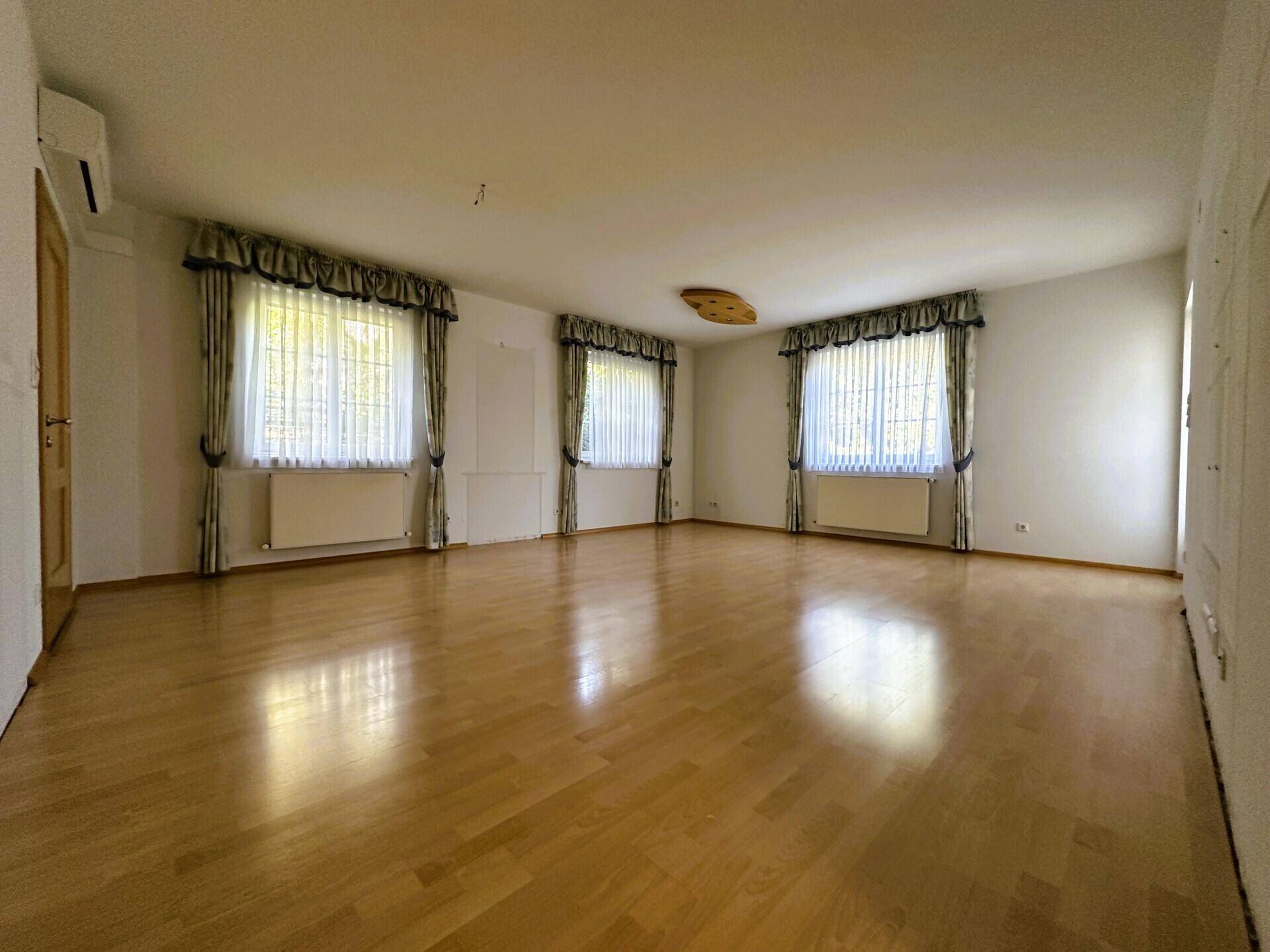 Helles Wohnzimmer mit Holzparkettboden, großen Fenstern und Klimaanlage.