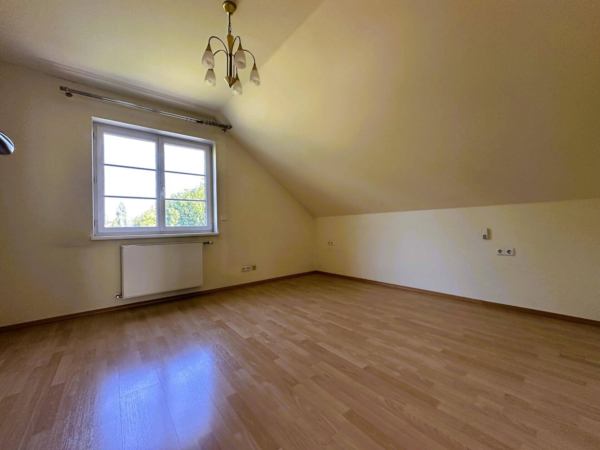Helles Schlafzimmer im Dachgeschoss mit Fenster und schrägen Wänden.