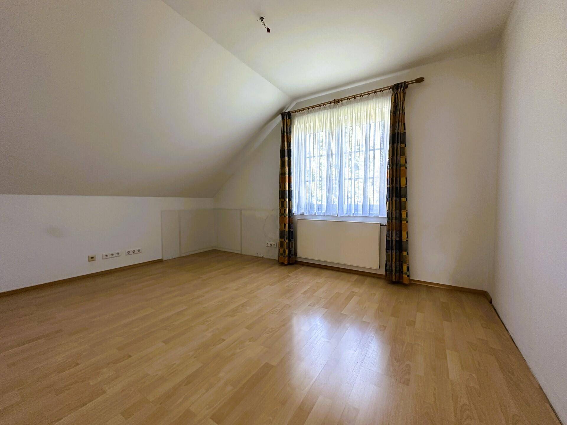 Gemütliches Schlafzimmer im Dachgeschoss mit Holzparkett und Fenster mit Vorhängen.