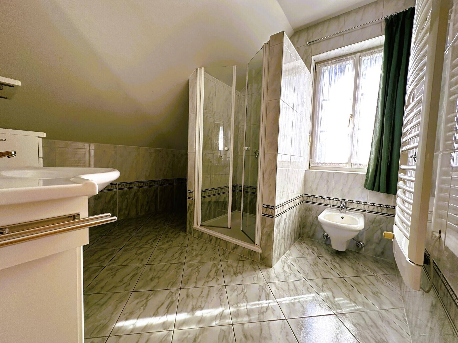 Badezimmer im Dachgeschoss mit Dusche, Bidet und gefliesten Wänden.