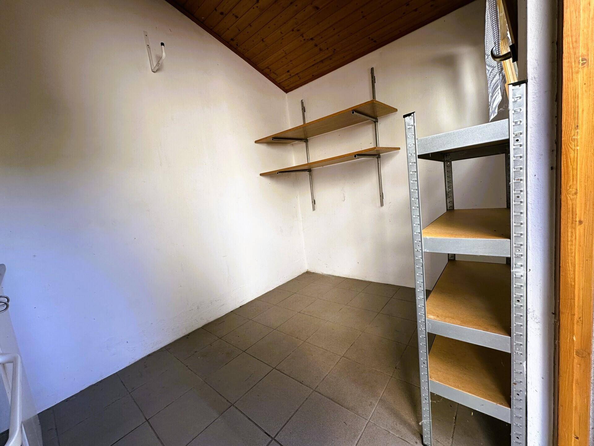 Kleiner Abstellraum mit Regalen und gefliestem Boden unter einer Holzdecke.