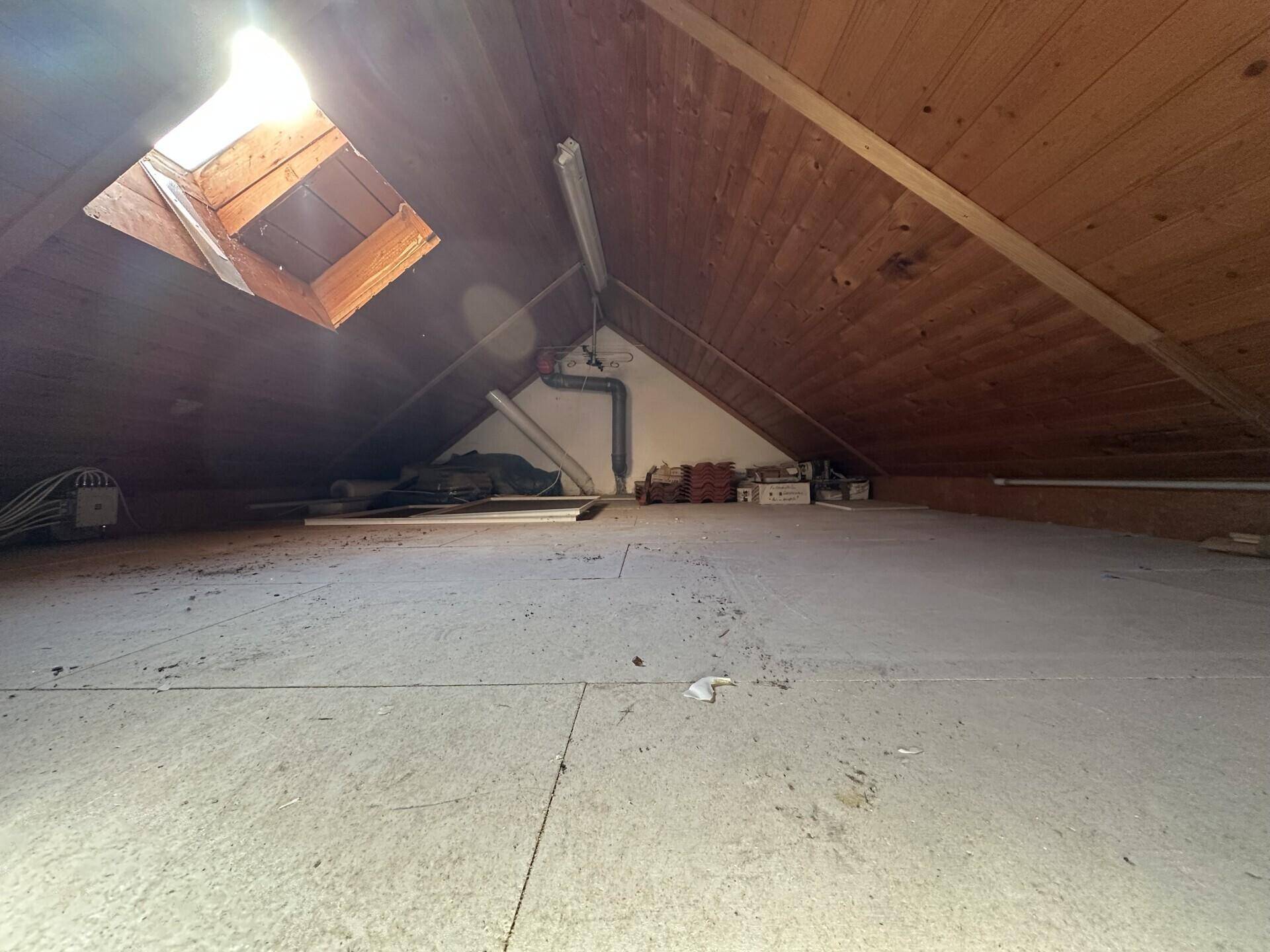Unausgebauter Dachboden mit Holzbalken und Dachfenster, ideal als Stauraum.