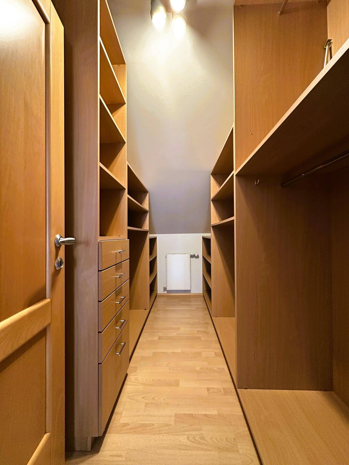 Begehbarer Kleiderschrank mit vielen Holzregalen und Stauraum.