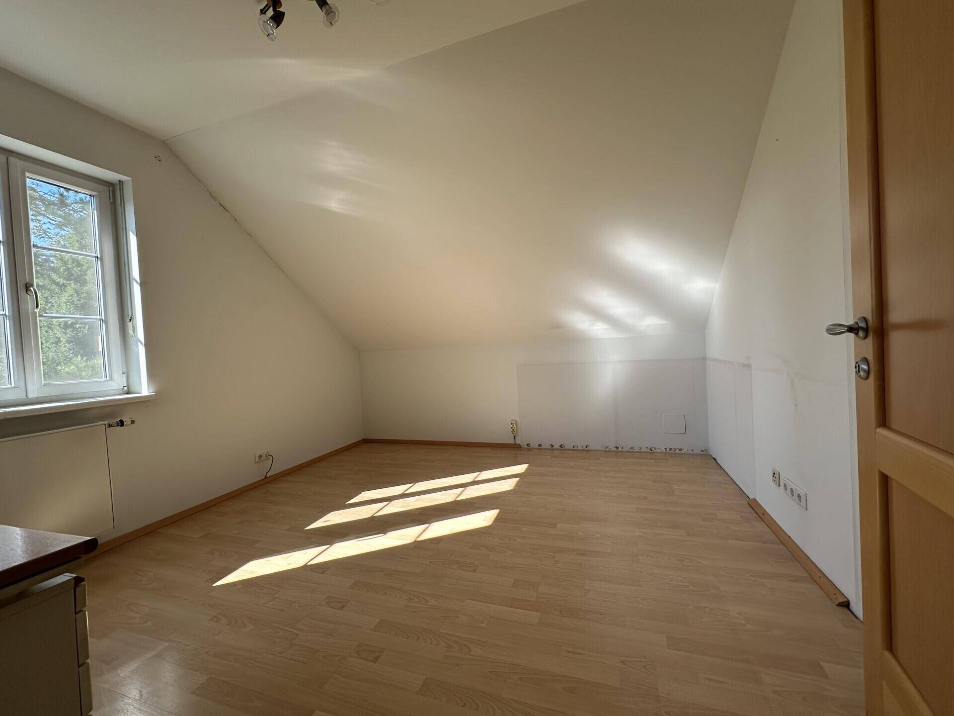 Lichtdurchflutetes Schlafzimmer im Dachgeschoss mit Holzparkett und schrägen Wänden.