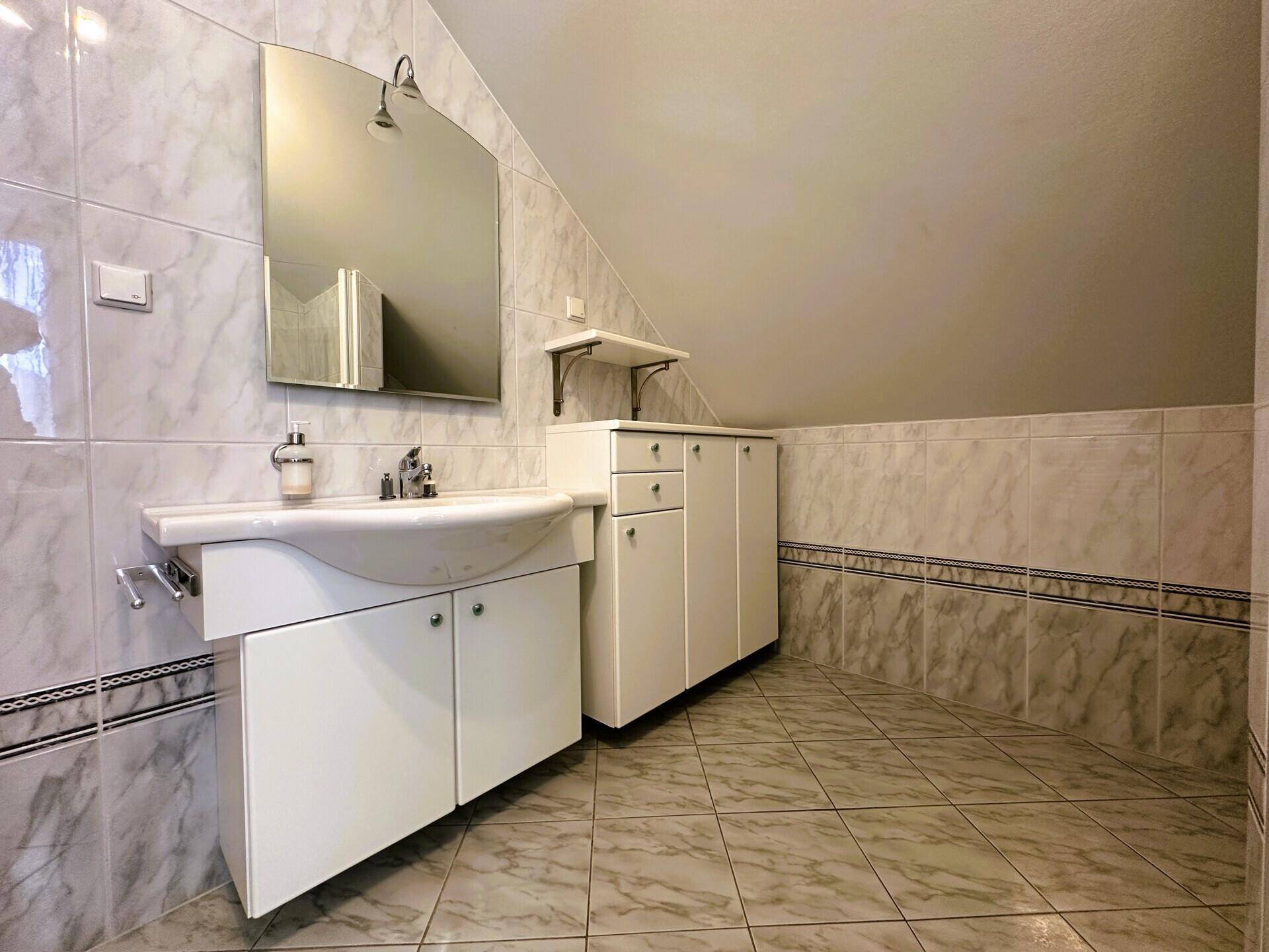 Badezimmer im Dachgeschoss mit Waschbecken, Spiegelschrank und gefliesten Wänden.