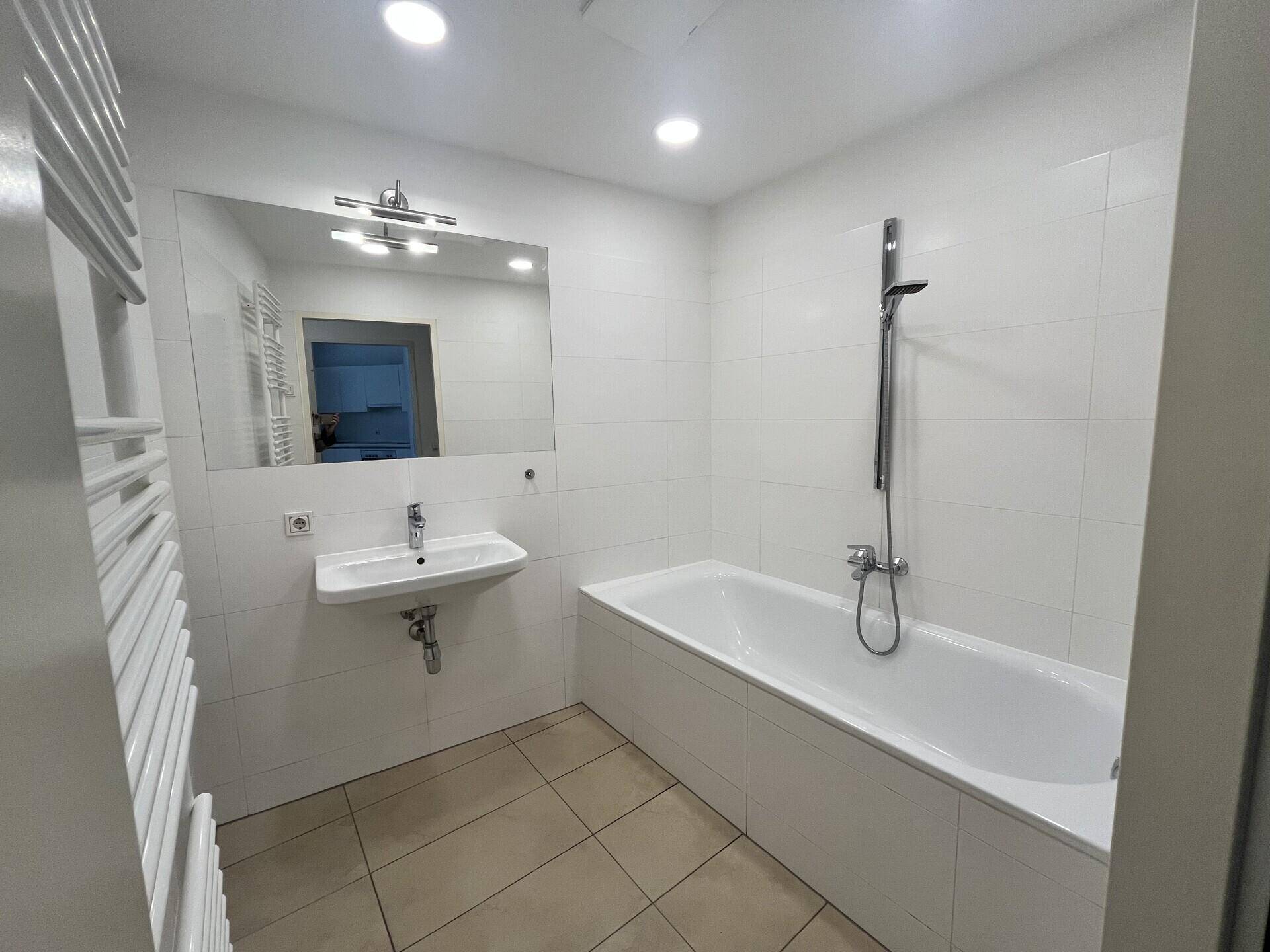 Helles Badezimmer mit Badewanne, Waschbecken und großem Spiegel.