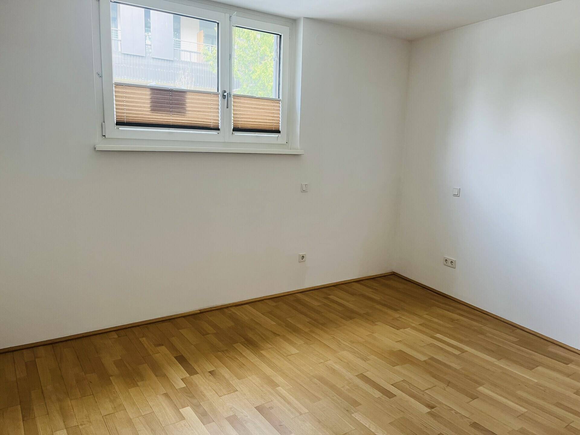 Helles Schlafzimmer mit Parkettboden und großem Fenster, bereit zur individuellen Gestaltung.